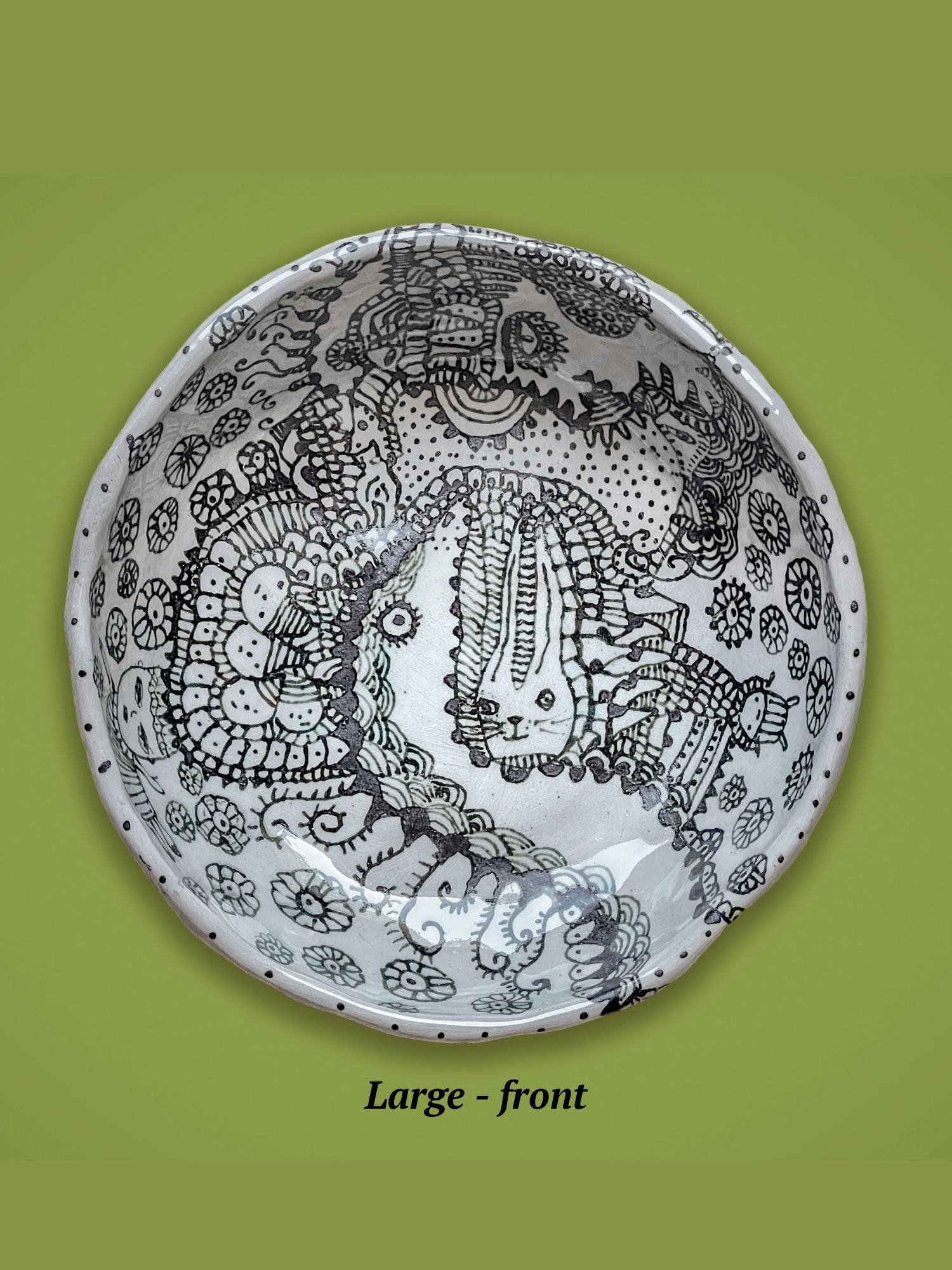 Decorative ceramic bowl with black patterns on a green background. The bowl is covered in fantastical illustrations with a cat in the center.