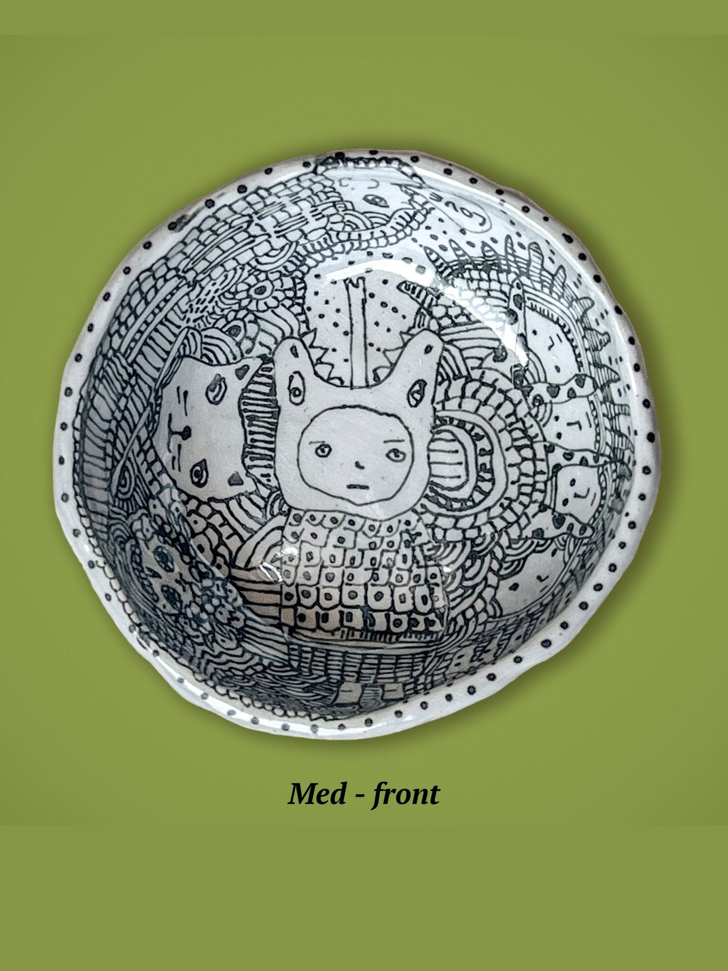 Decorative bowl with black and white patterns on a green background. A face is in the center surrounded by a mix of lines and other faces. The rim is dotted.