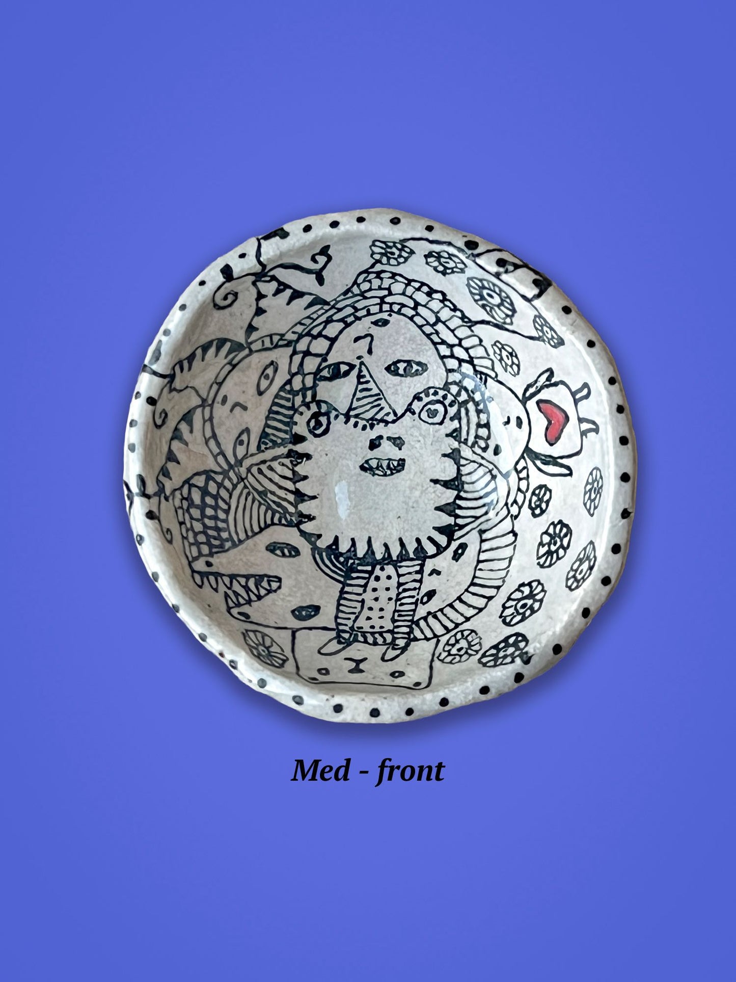 A smaller ceramic bowl with artistic designs created in black. One figure is a small girl with a red heart on her chest.
