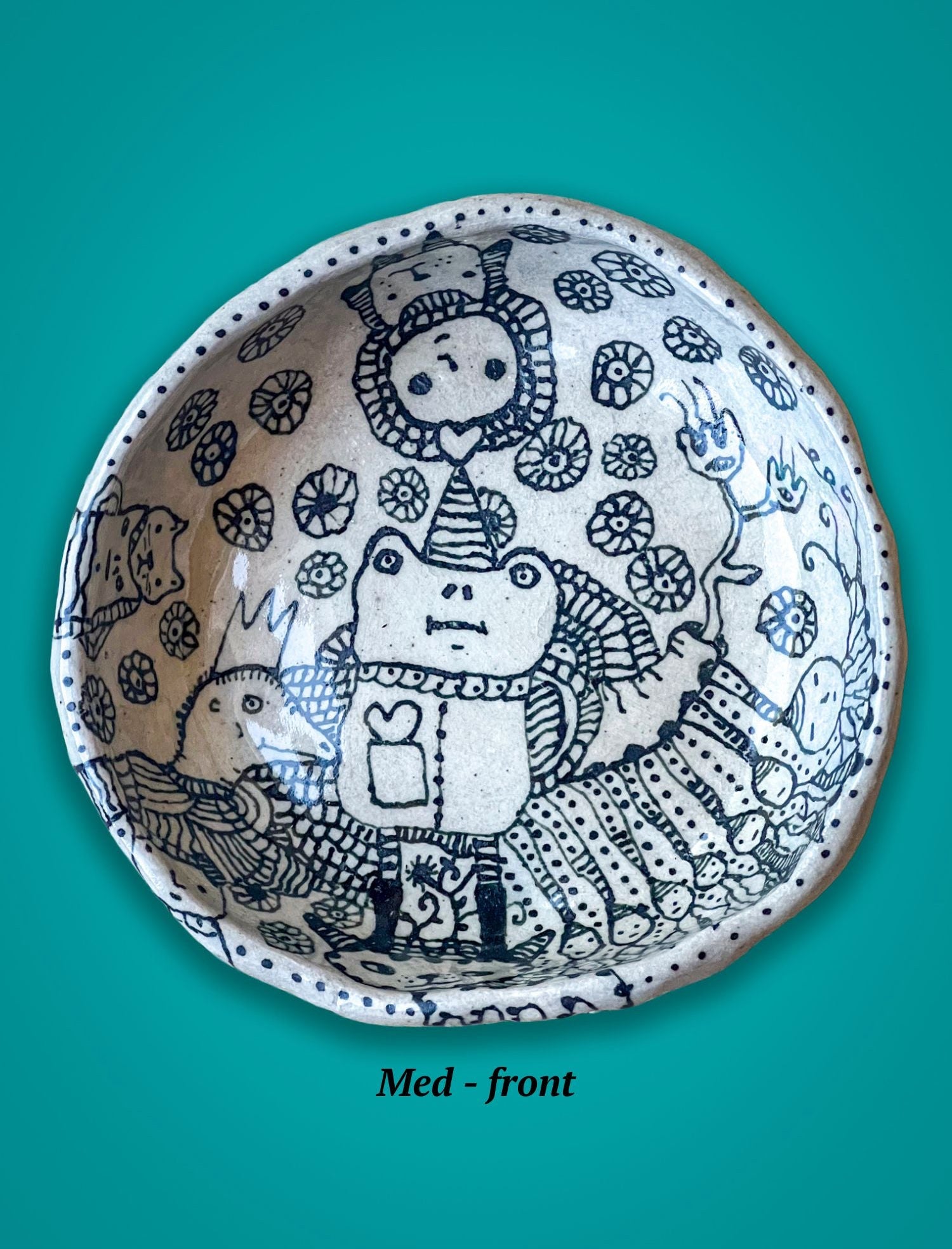 Ceramic bowl with black line art design on a teal background. The figures are whimsical creatures with flowers.