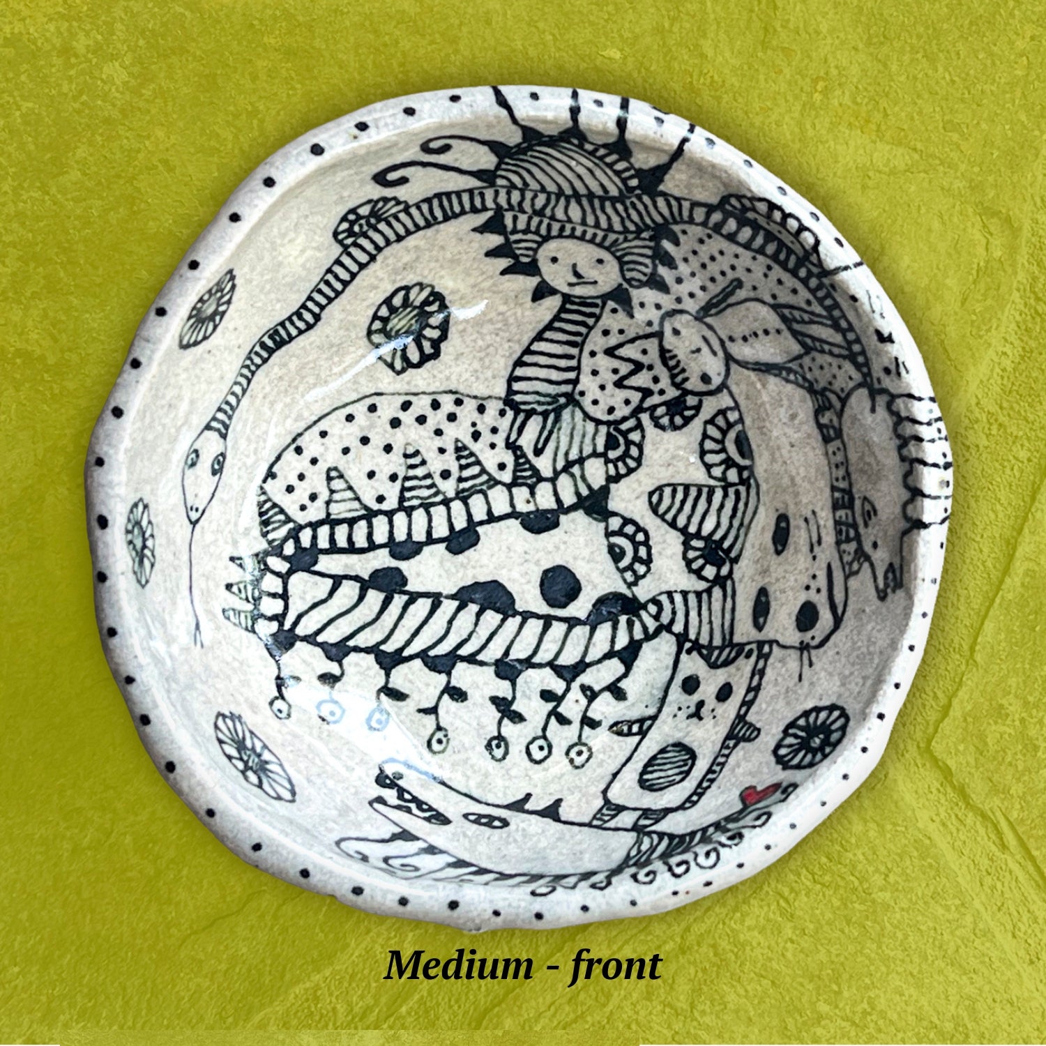 Decorative bowl with black line art with whimsical creatures including a snake and a cat.