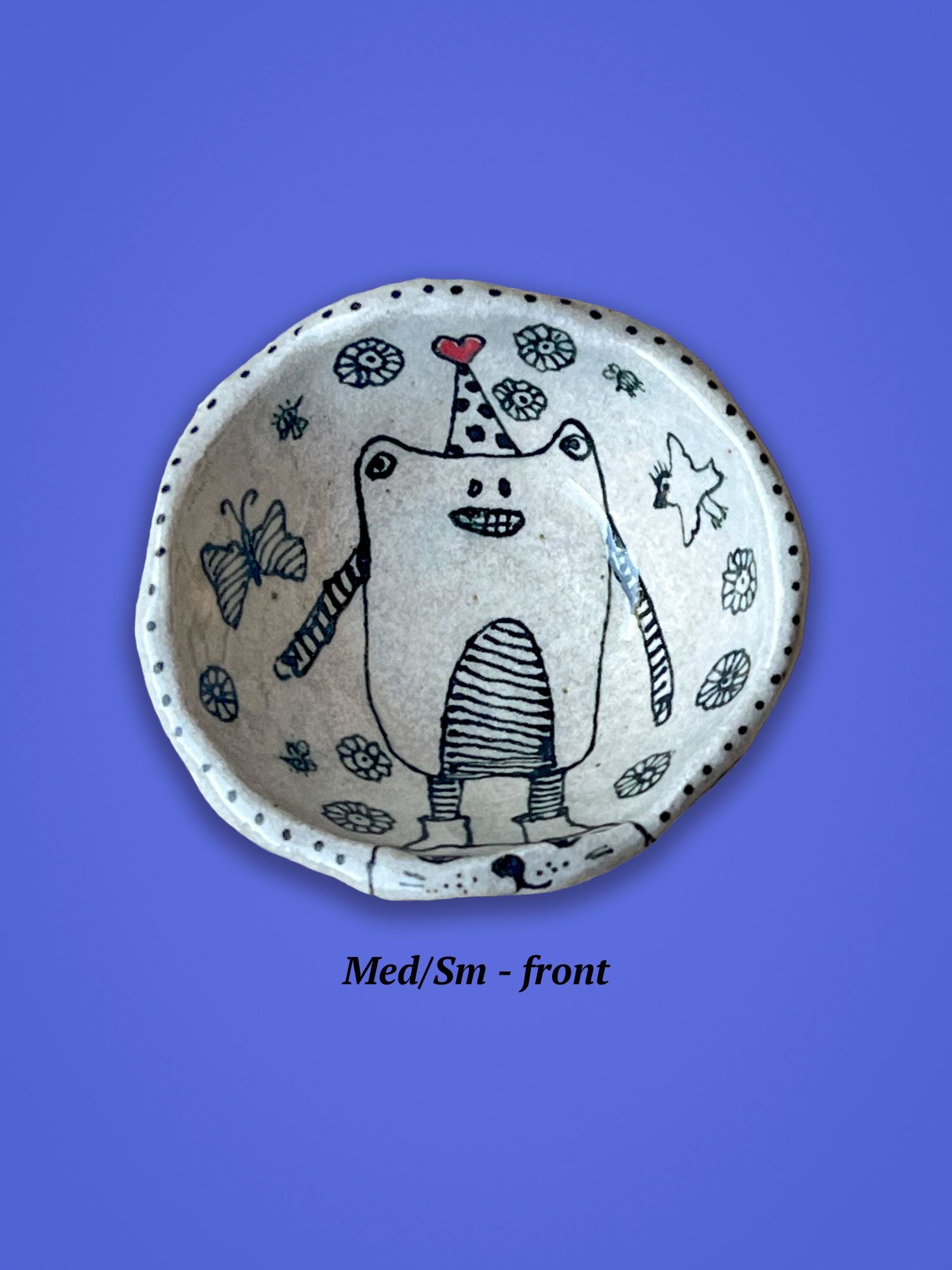 A small ceramic bowl with a cartoon bear design in its center. It is wearing a tall hat with a red-heart on top.