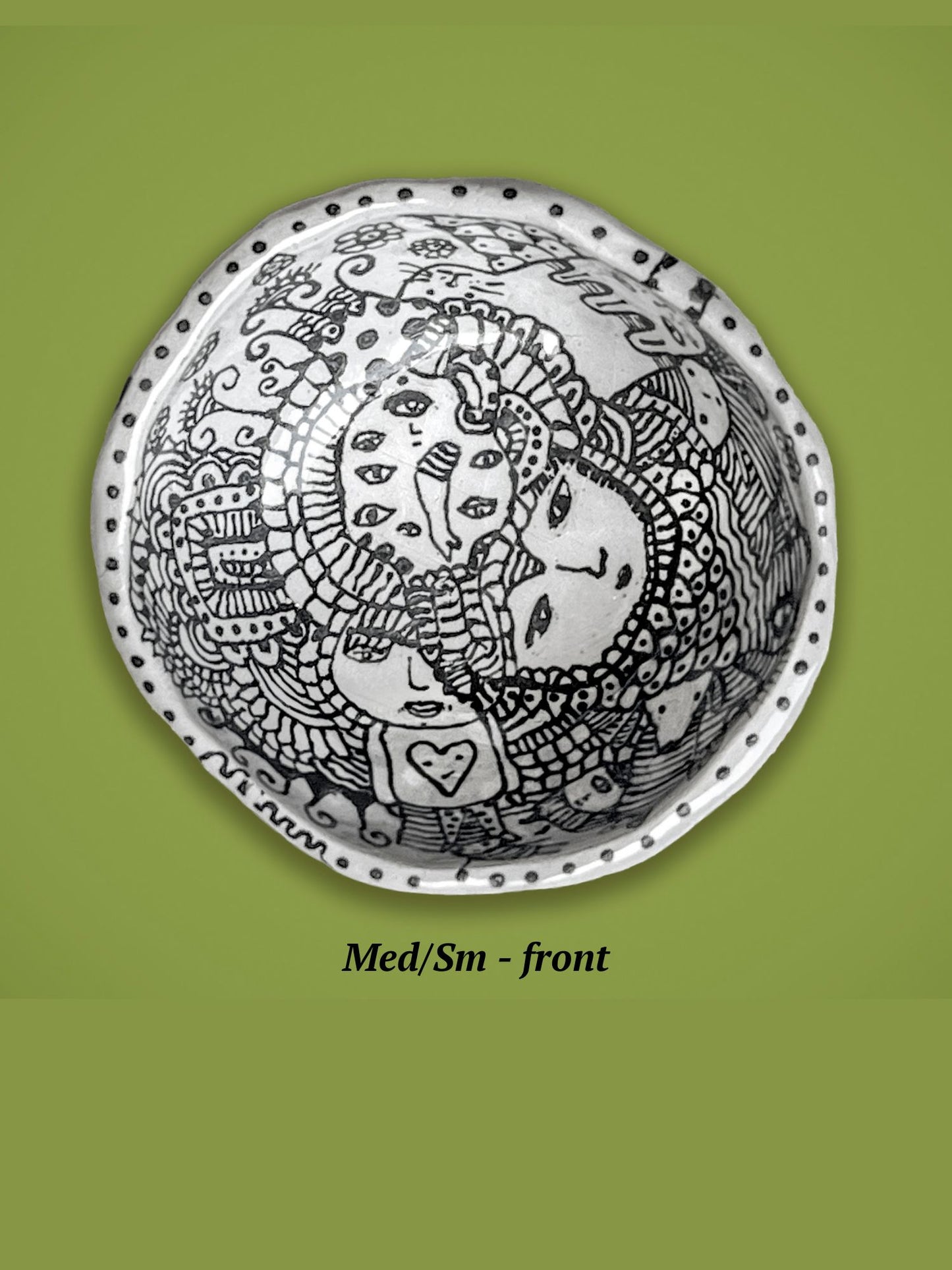 Decorative ceramic bowl with black drawing. It sits on a green background. There is a collage of faces in the center.