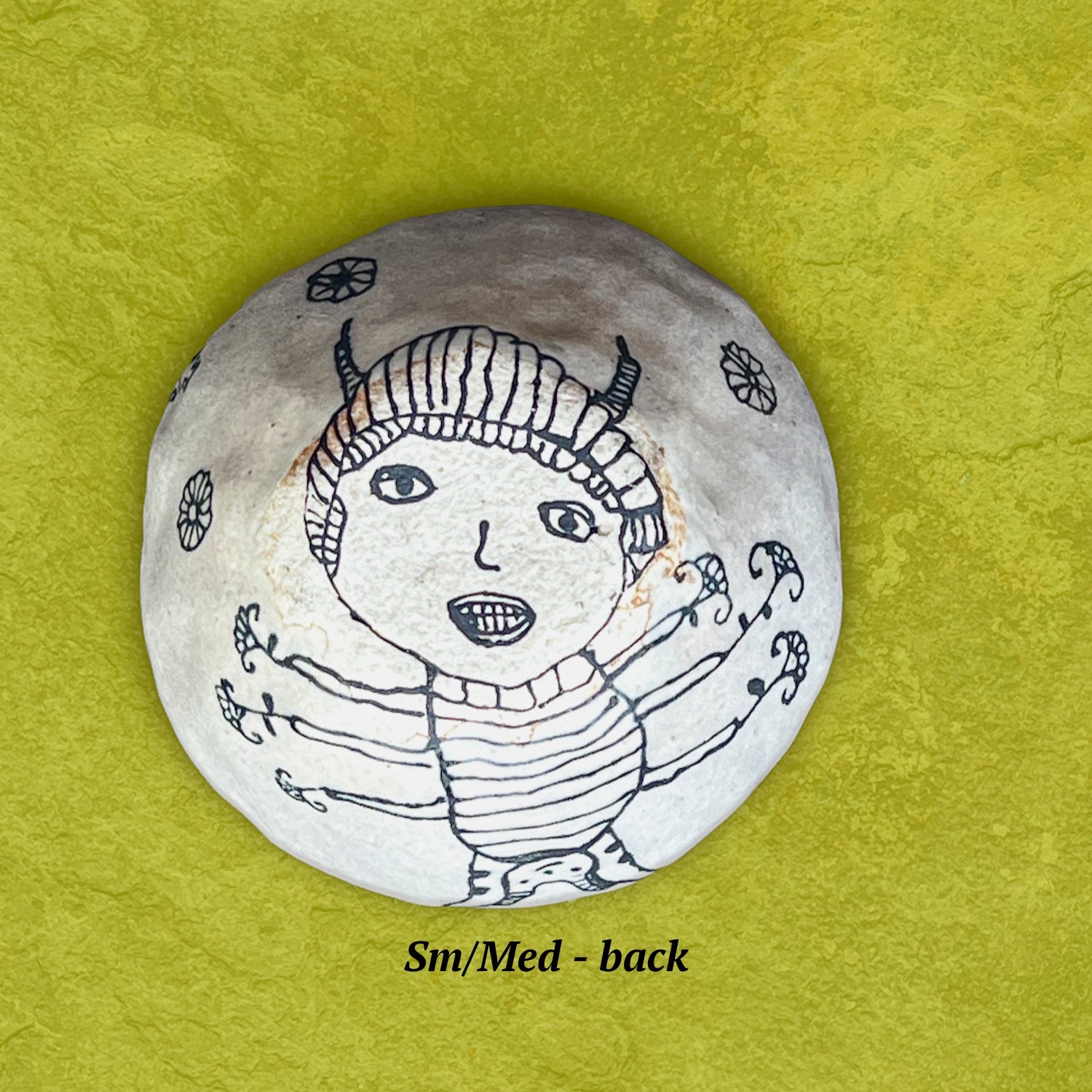 The backside of a bowl showing a black and white illustration of a creature with several arms holding flowers.