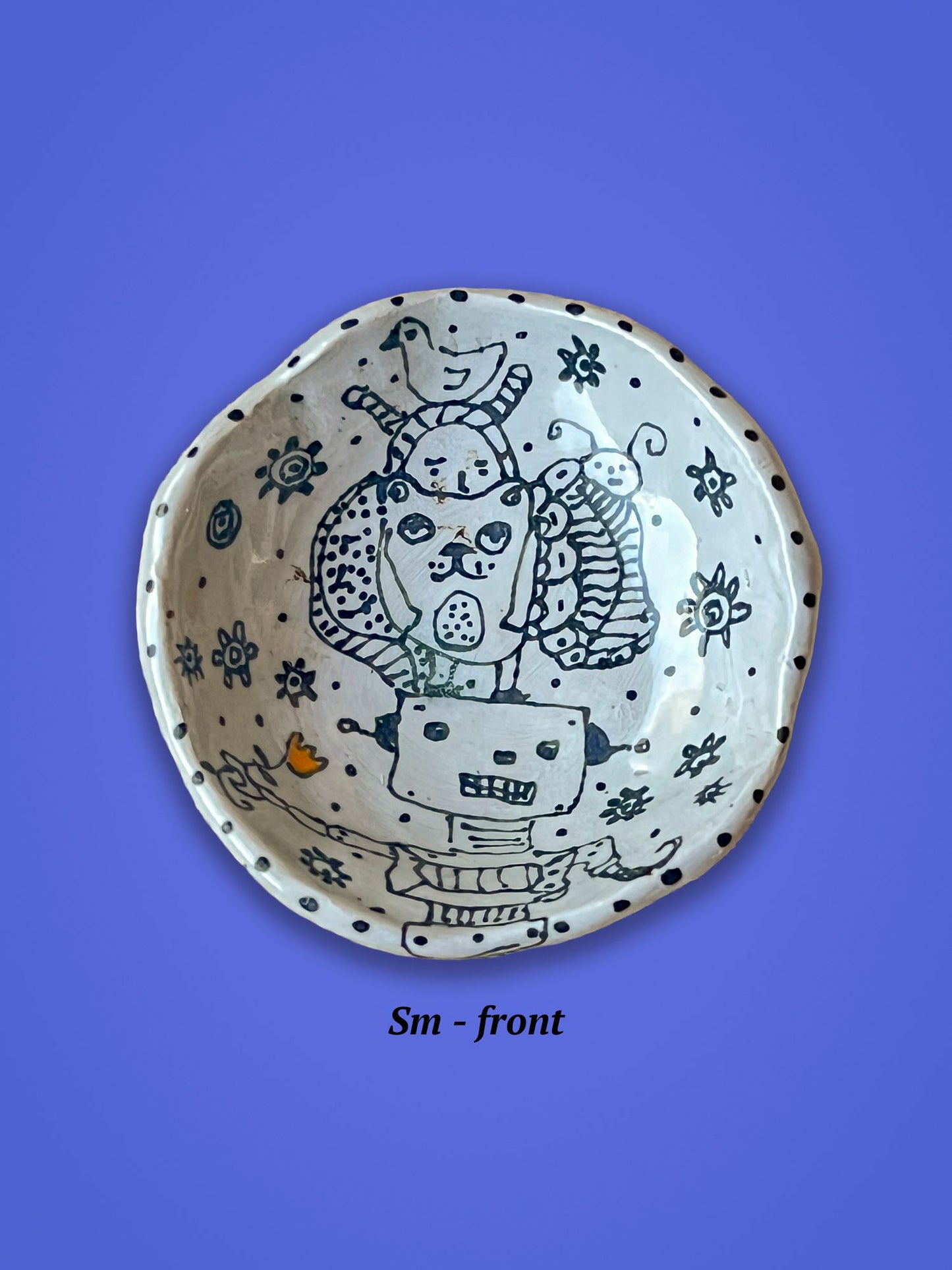 Small ceramic bowl with artistic design of a dog, a duck and robot. There is a small red flower that is a spot of color as the rest of the illustrations are black on white.