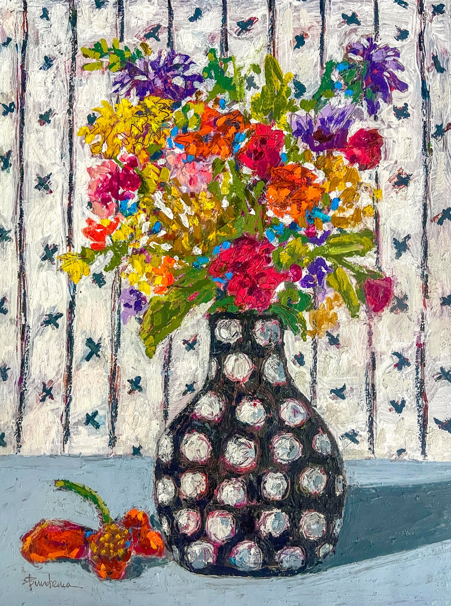 Pattern and color are the hallmarks of this floral still life painting. A black and white polka dot vase, sits on a table against a patterned wallpapered background. The bouquet looks to be a bunch of wildflowers, with a lone flower that has dropped and lays on the table.