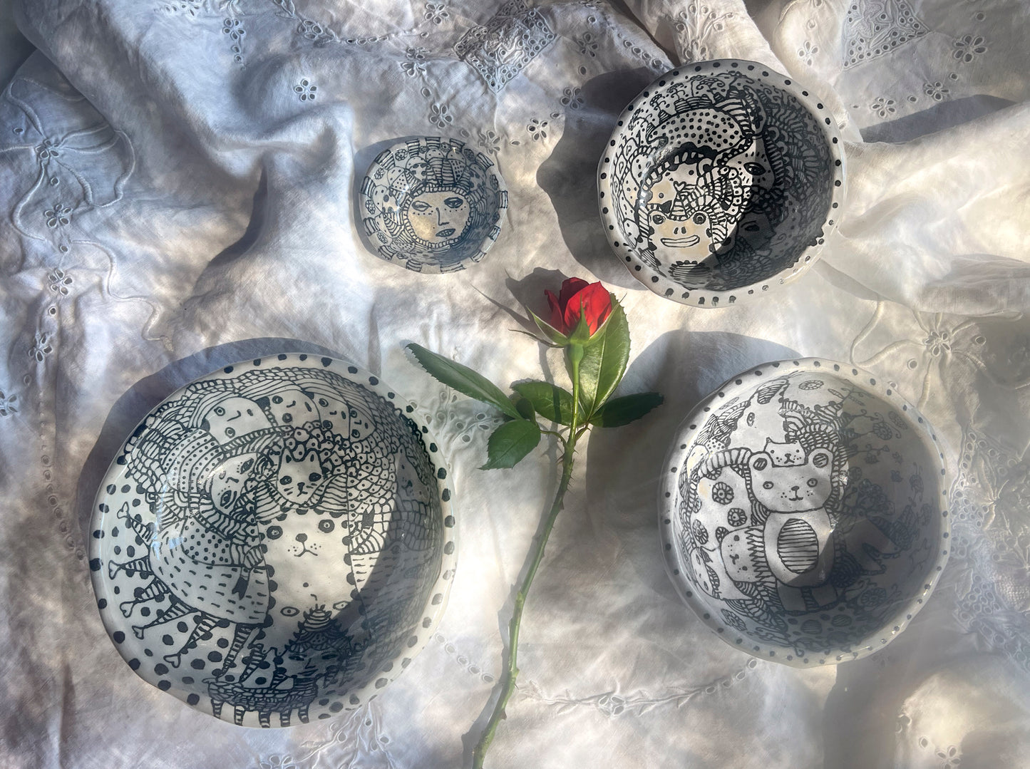 Decorative bowls with intricate black and white design are shown here on a textured surface with a red rose.