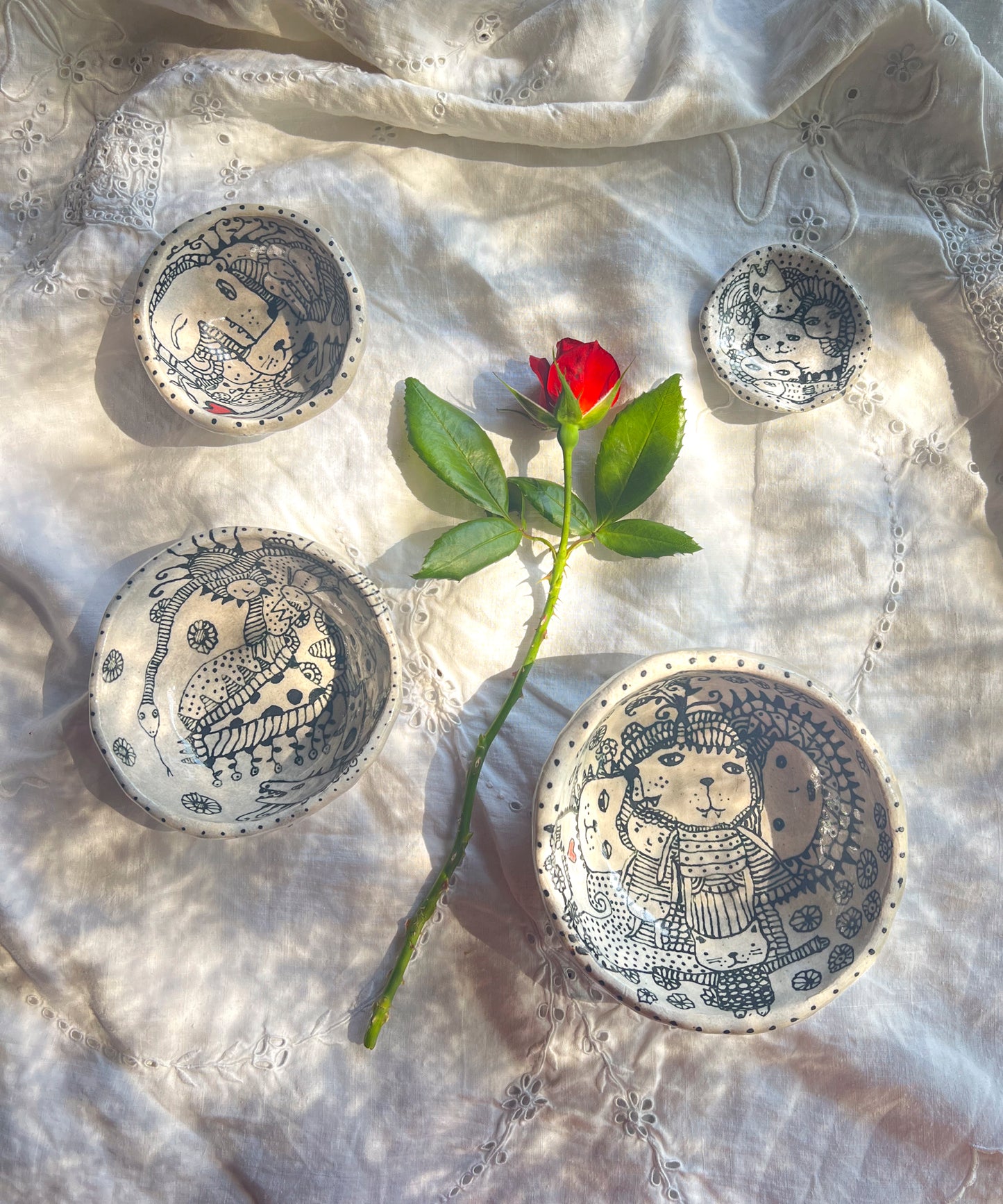 Decorative bowls with intricate designs on a textured fabric background. Four bowls are each drawn with whimsical characters.