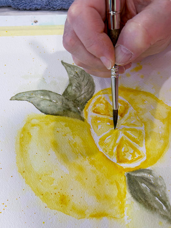 Artist's hand with paint brush painting lemons