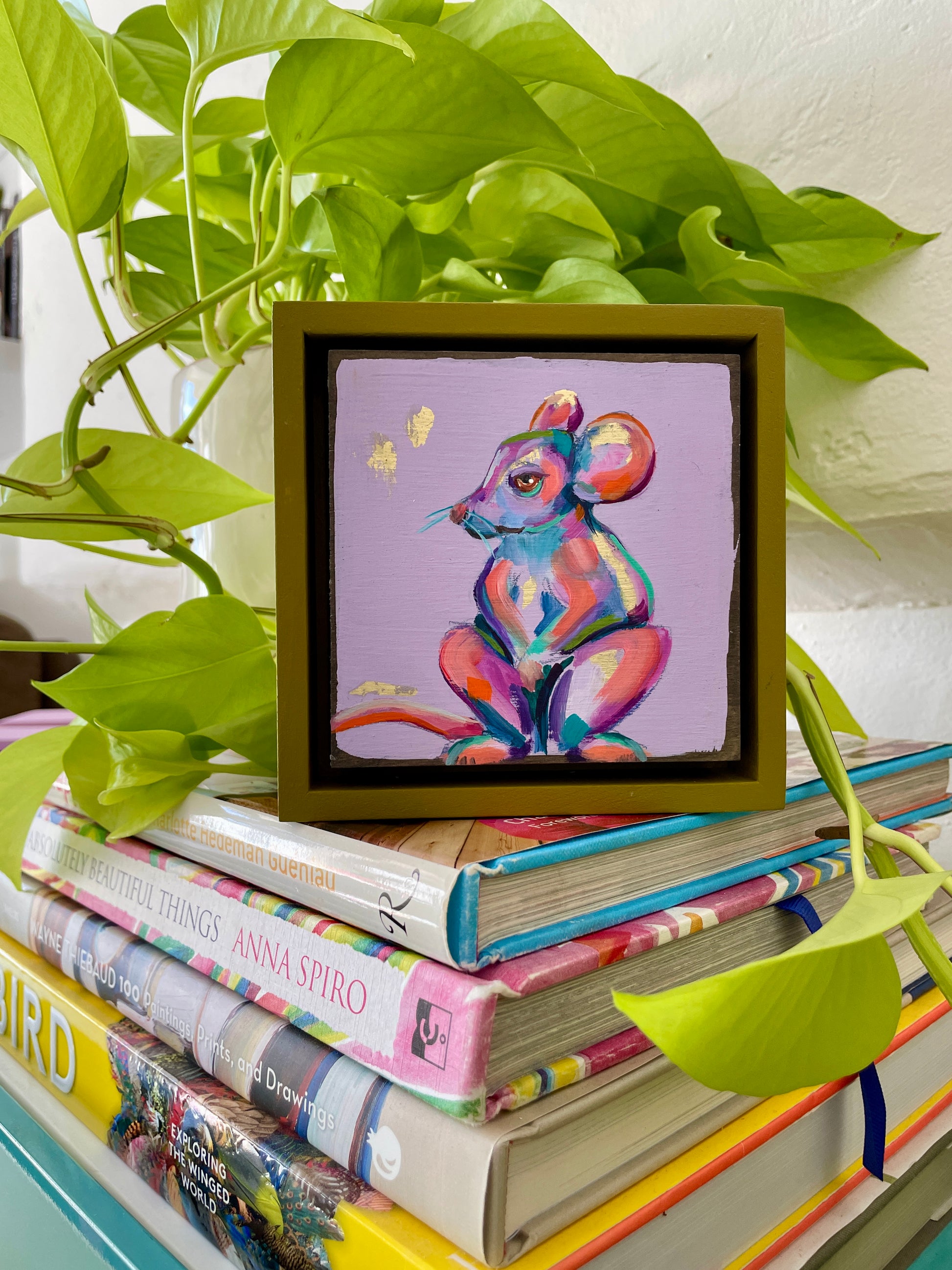 Colorful whimsical painting of a mouse in blues, purples, pinks with touch of gold leaf; 5"x5" incl painted frame; placed on top of stack of books; artist Shaney Watters