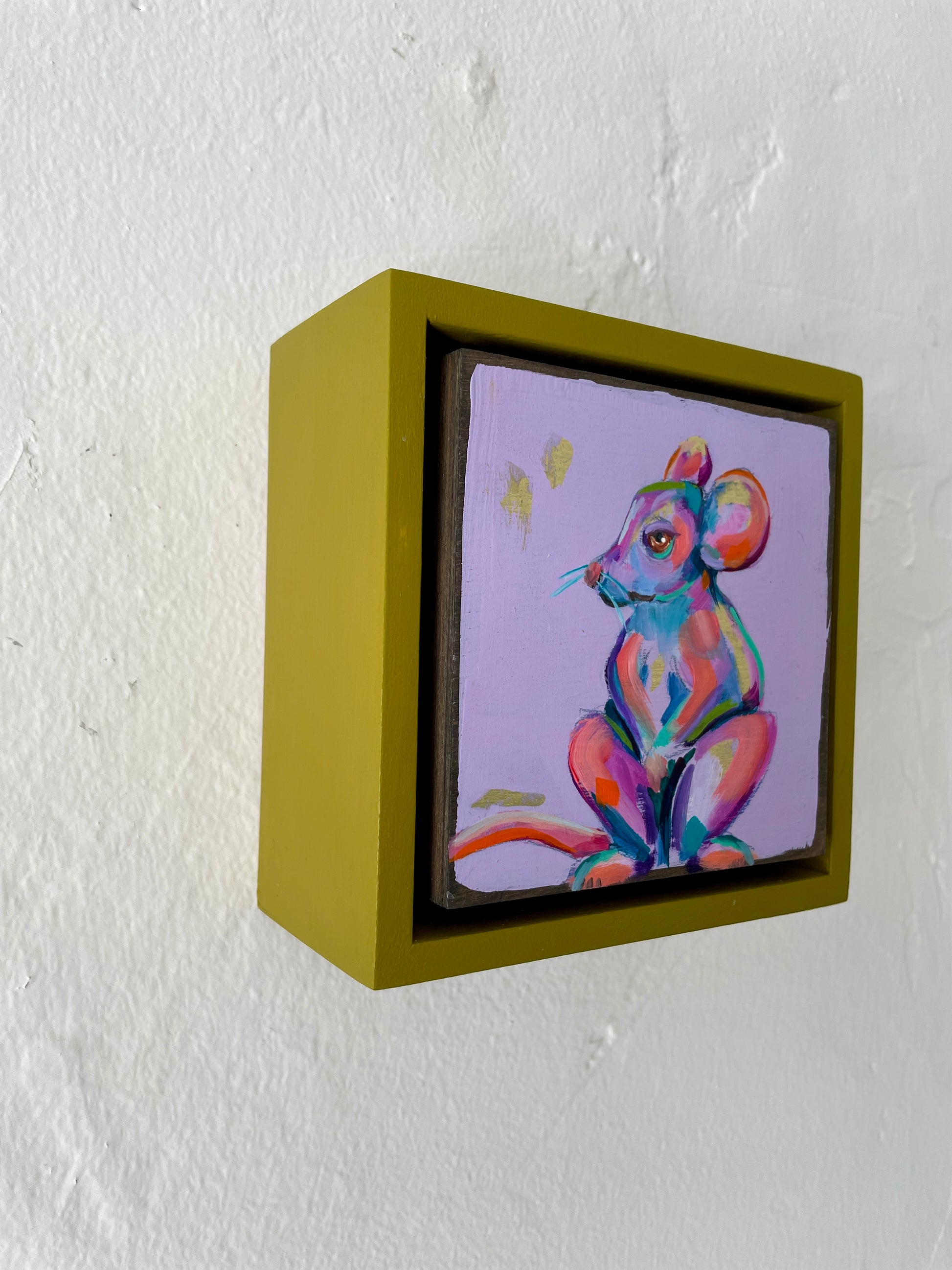 Colorful whimsical painting of a mouse in blues, purples, pinks with touch of gold leaf; 5"x5" incl painted frame; artist Shaney Watters; side view on wall