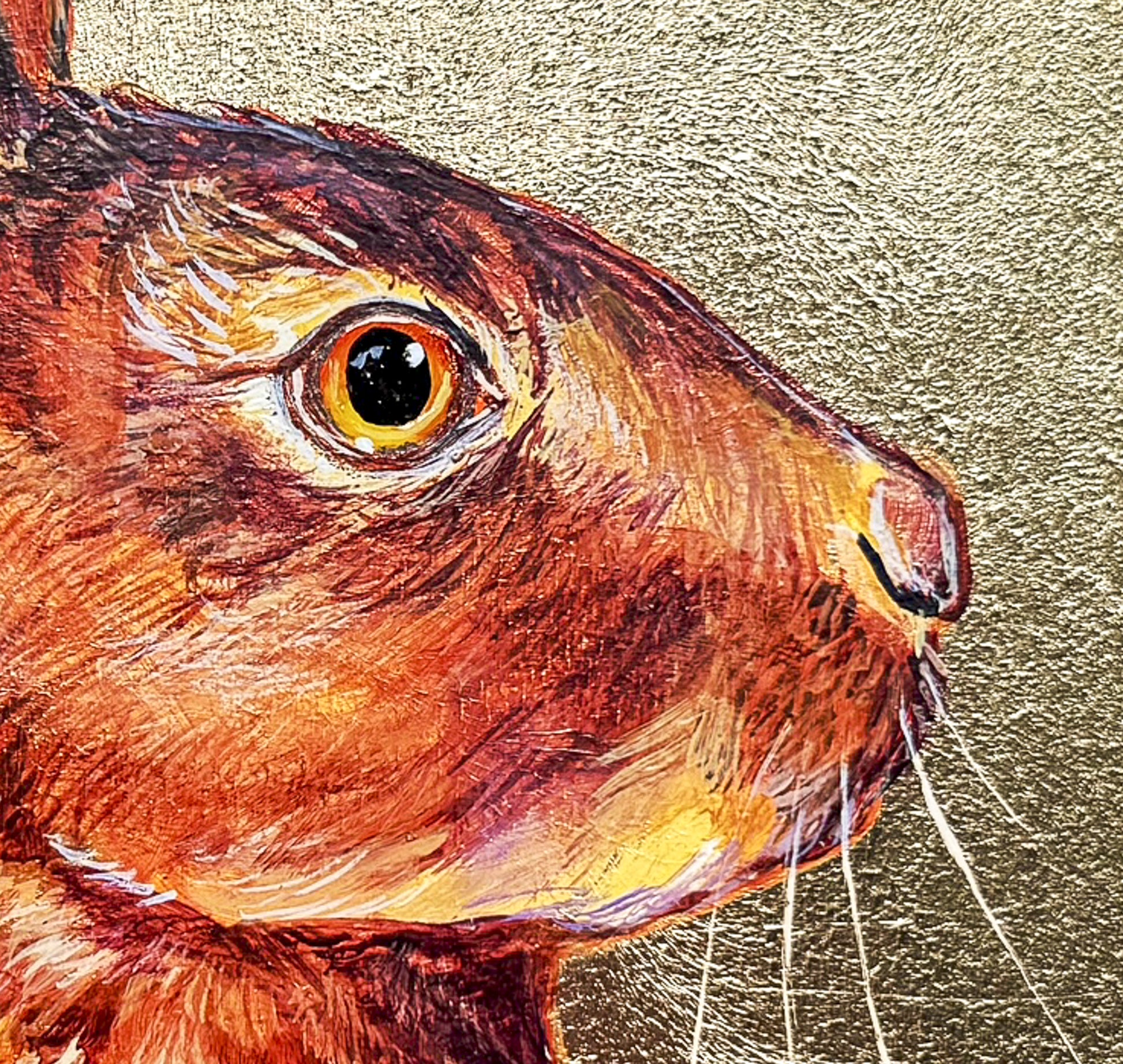The detail of the rabbit's head, eyes and whiskers is featured in this close up image. The rabbit is painted in hues of brown, orange, yellow and white. The background is gold leaf.