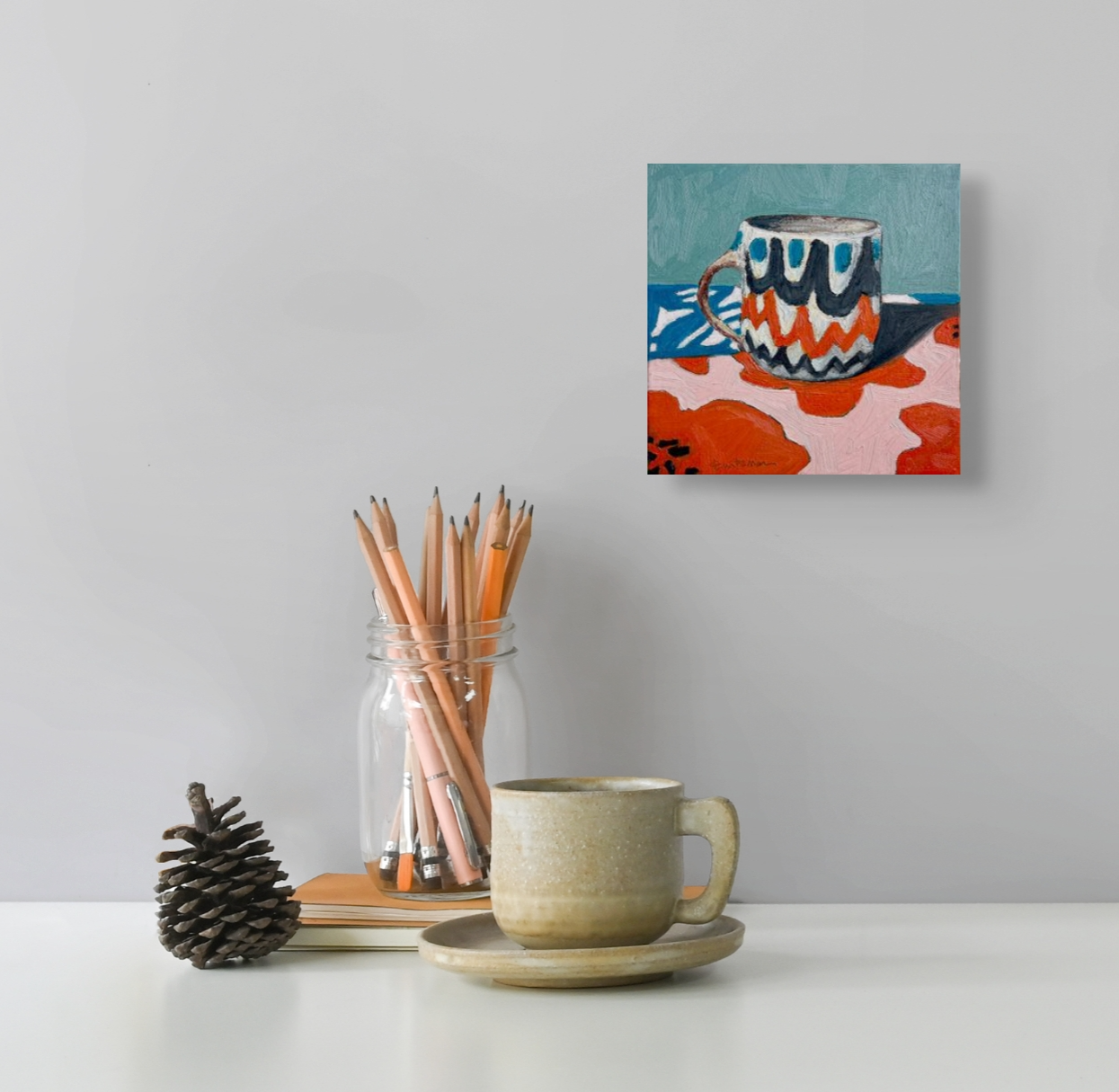 Morning Witness hangs on a light gray wall over a counter. On the counter sits a coffee mug, jar of pencils and a pine cone.