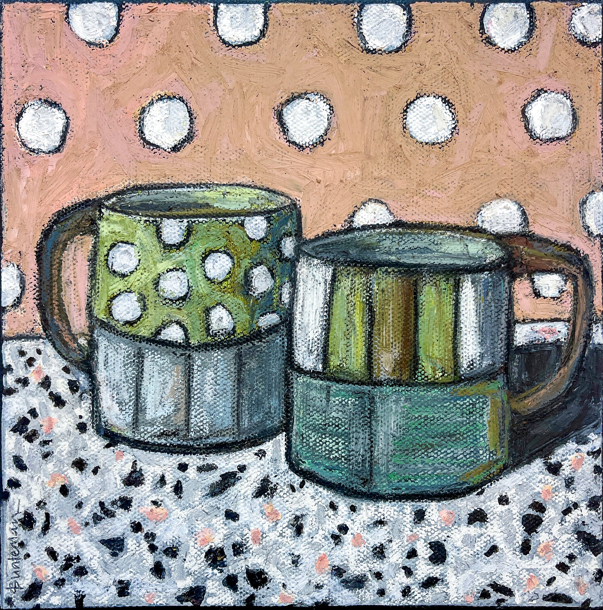 Two mugs, not matching but coordinated in colors of green, gray and white, sit on a marbled tabletop. The background is a light pink with white polka dots which match the white dots on one of the mugs.