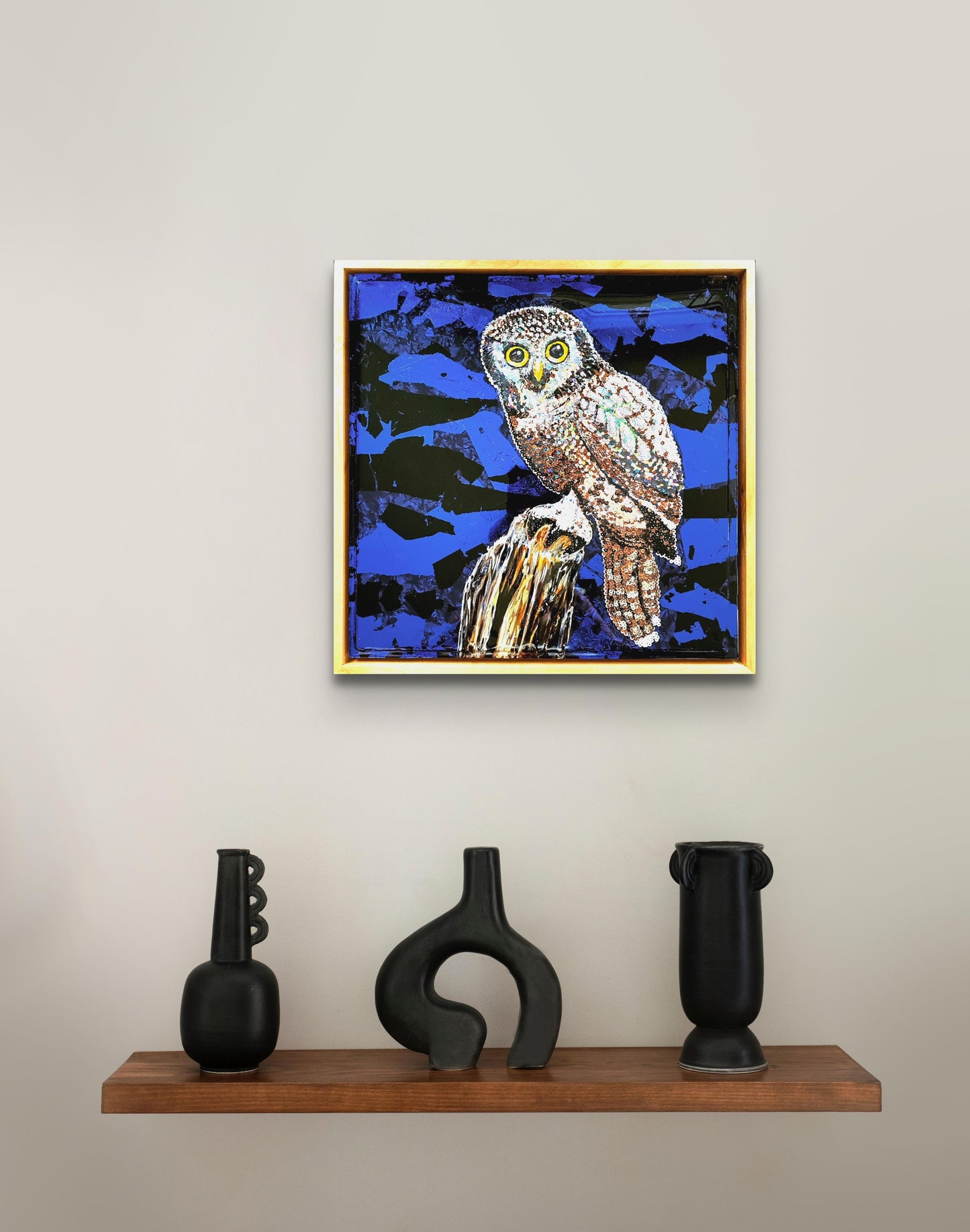 Colorful acrylic painting of owl on blue background; owl is comprised of various colored sequins; resin coating on top; artist Marie Lavallee; shown on wall in situ