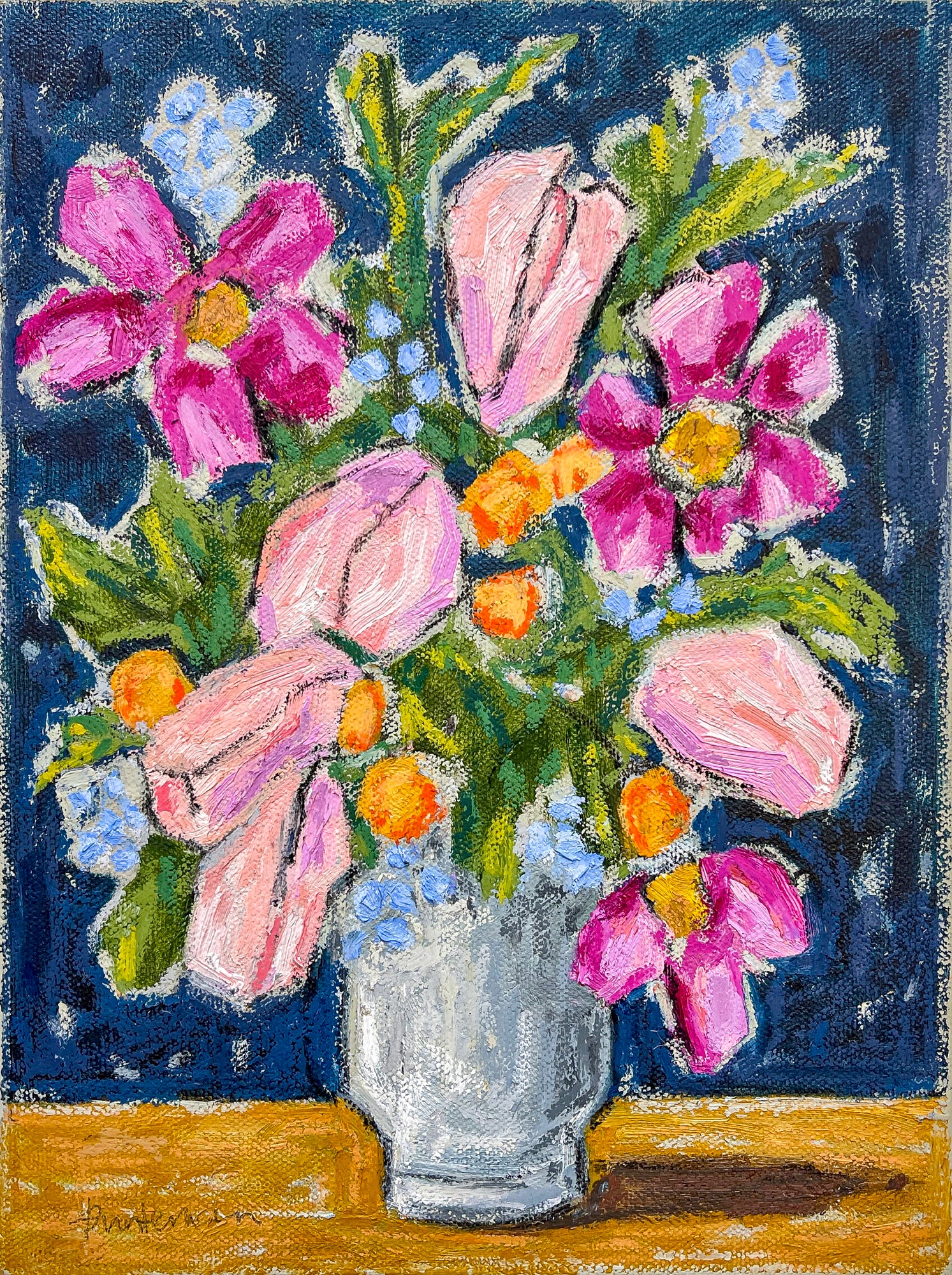 This is a beautiful still life of a mixture of flowers in a white base against a blue background. The flowers are of a mixed variety in pinks, oranges and dark pink. We also see the green foliage.