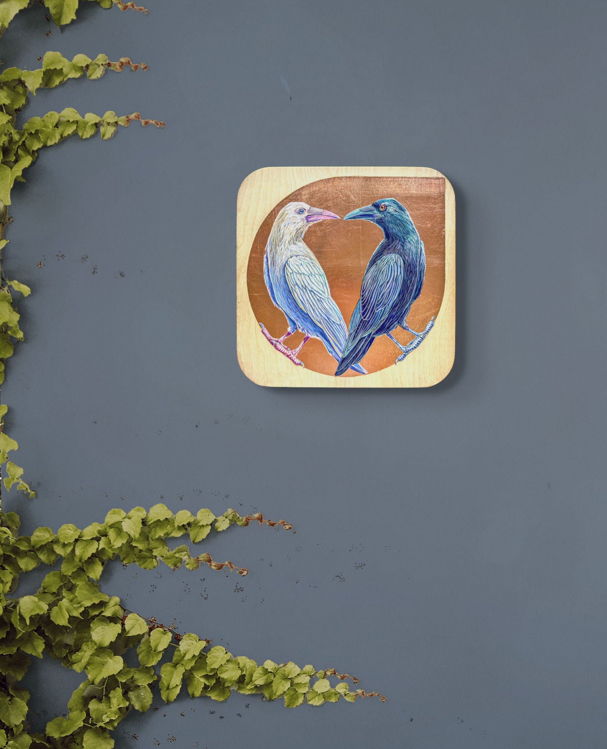 Two painted ravens, one white and one black, turning face to face. Painted against a copper leaf background on natural birch wood; artist Marie Lavallee; shown on wall in situ