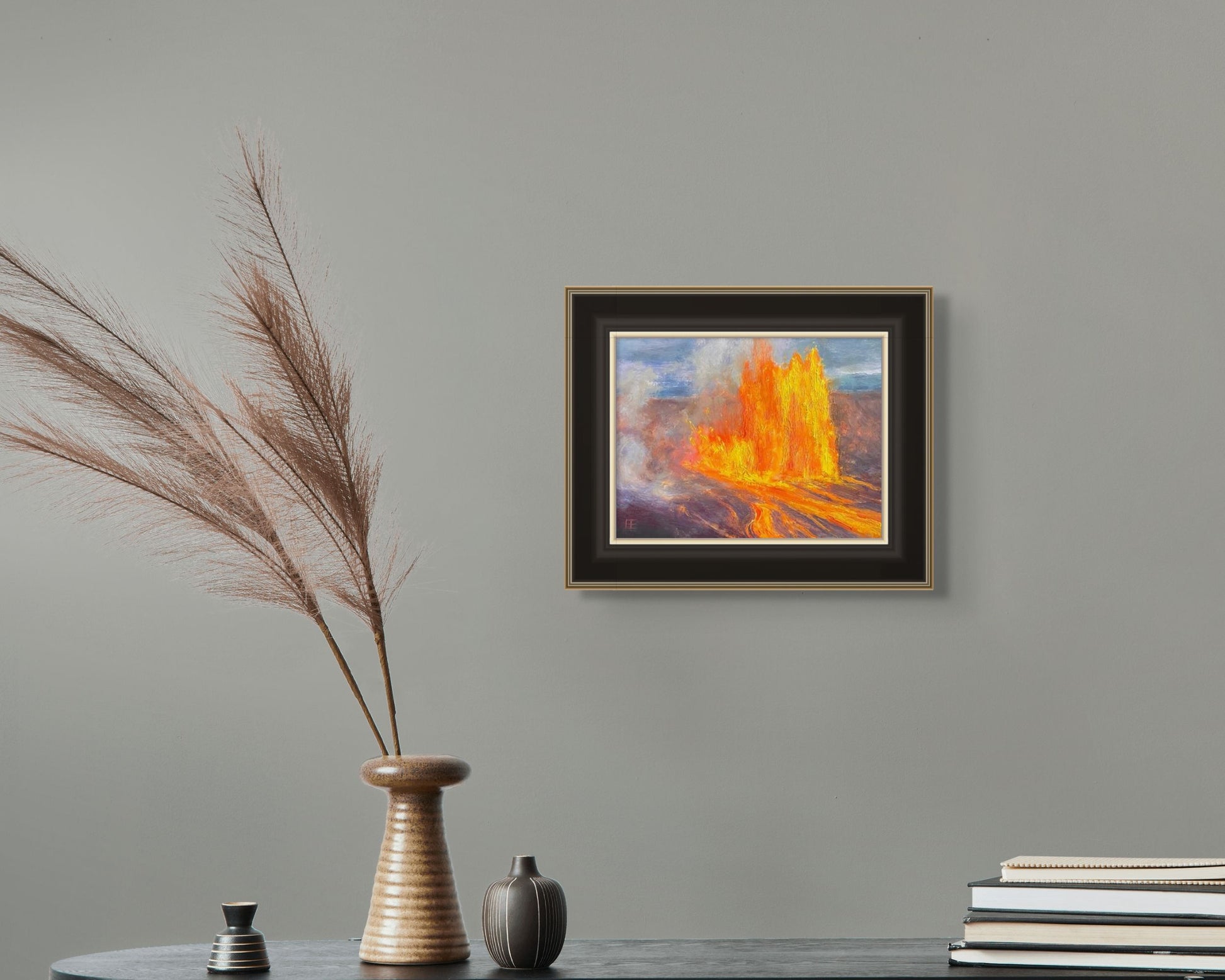 Always Kilauea 2025 is shown here in in-situ hanging on a pale blue/green wall over a small table. The table is adorned with a vase with a dried wheat stem and a few stacked books.