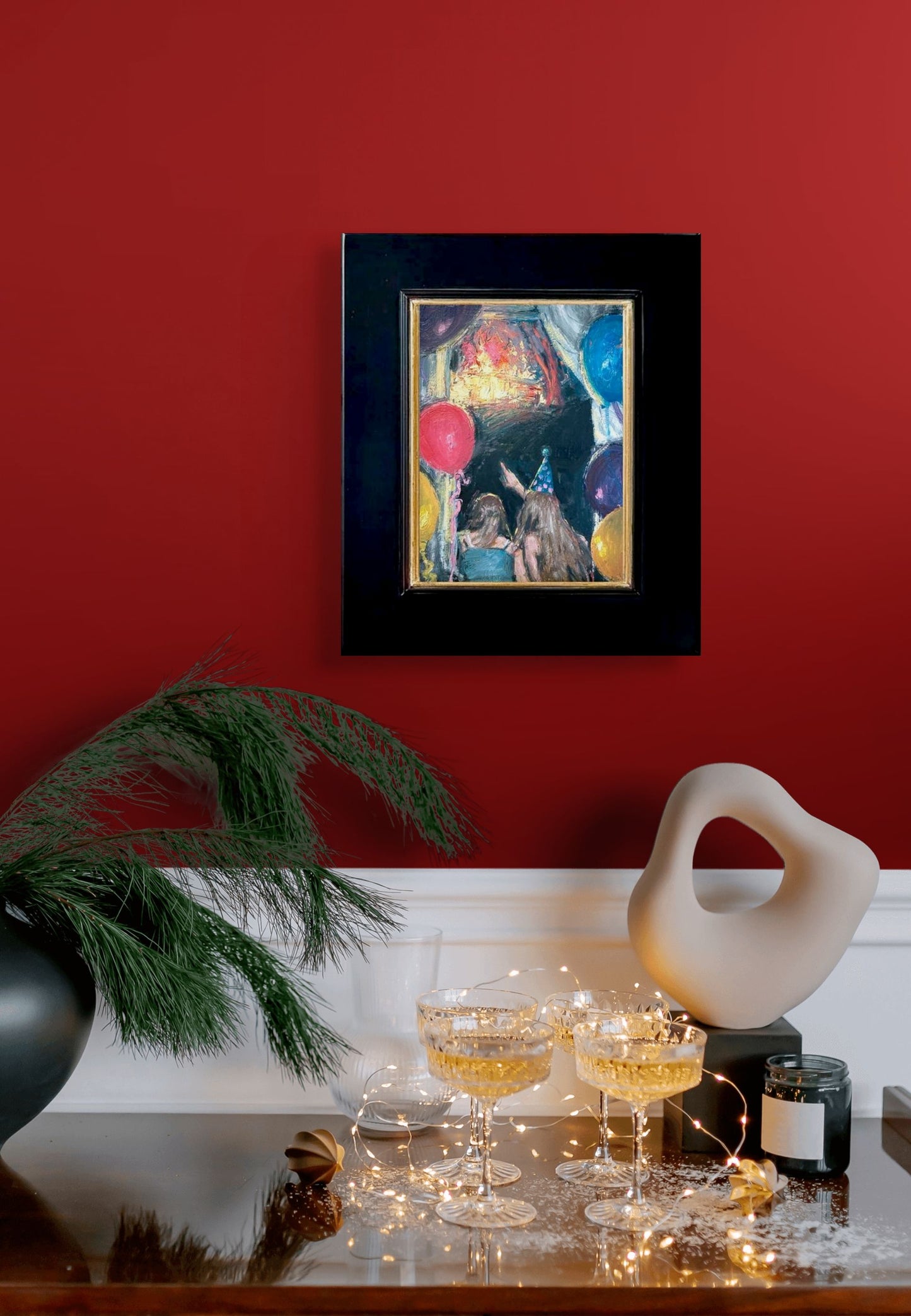 Impressionistic depiction of two people with party hats and balloons against a dark background looking and pointing at a lighted stage; shown with 2" black wood frame and gold lining; shown on red wall above shelf with tiny lights and bubbly drinks