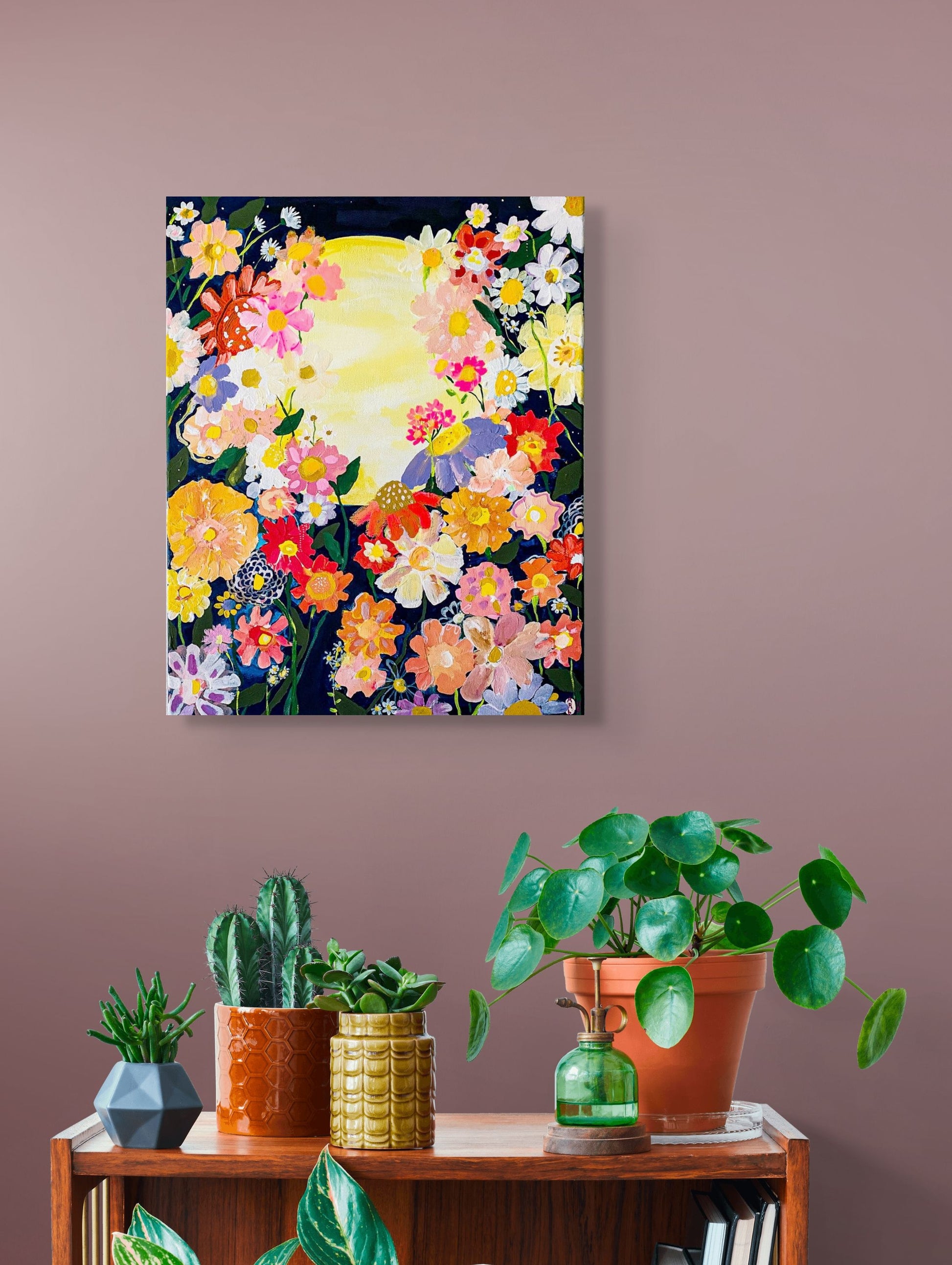 Colorful flowers provide a beautiful border for a bright yellow full moon on a starry dark sky background; shown in situ against taupe wall with potted plants below.