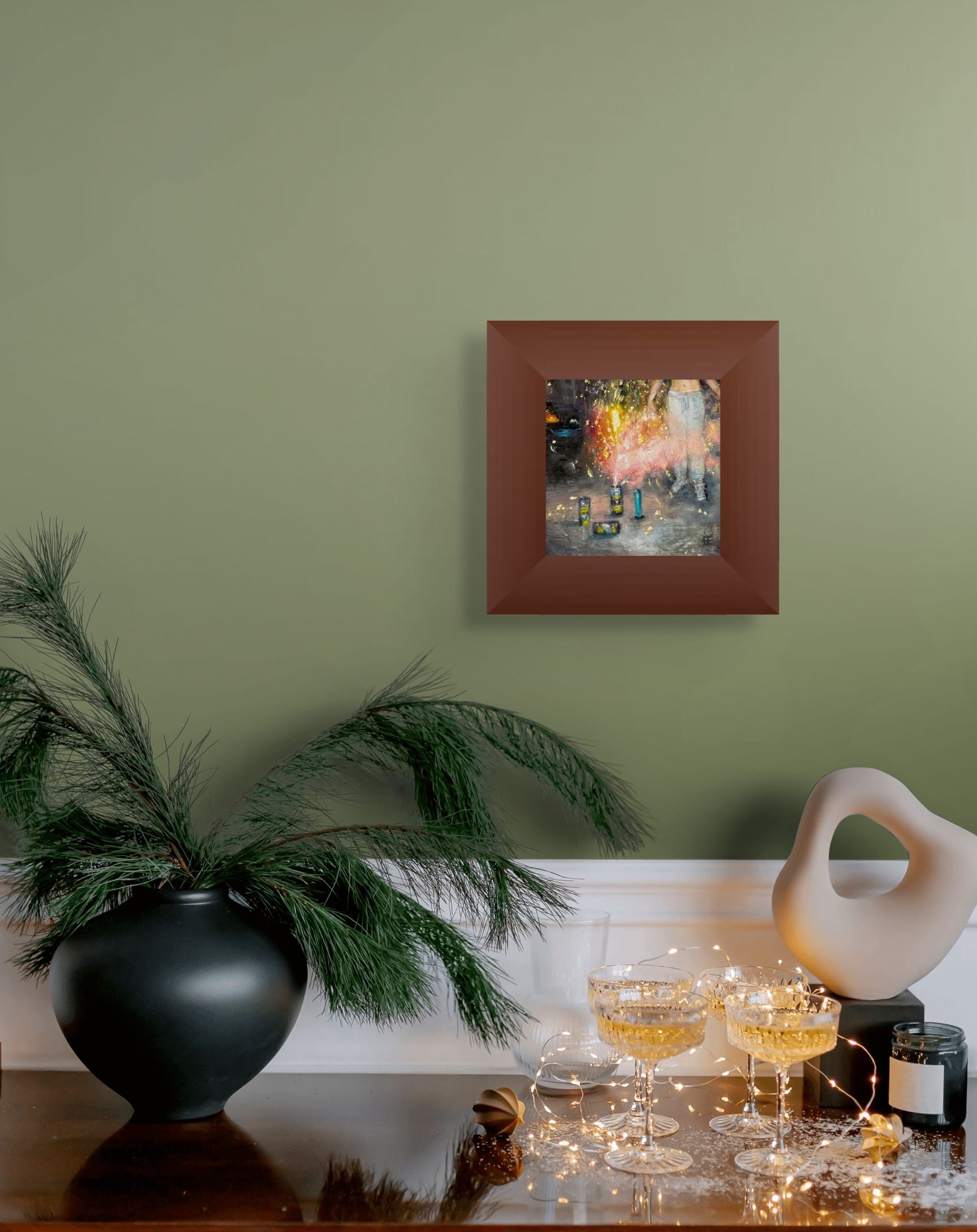 This image shows the painting on a wall of green over a counter with filled wine glasses and a plant. The painting is framed in a wide brown wooden frame.