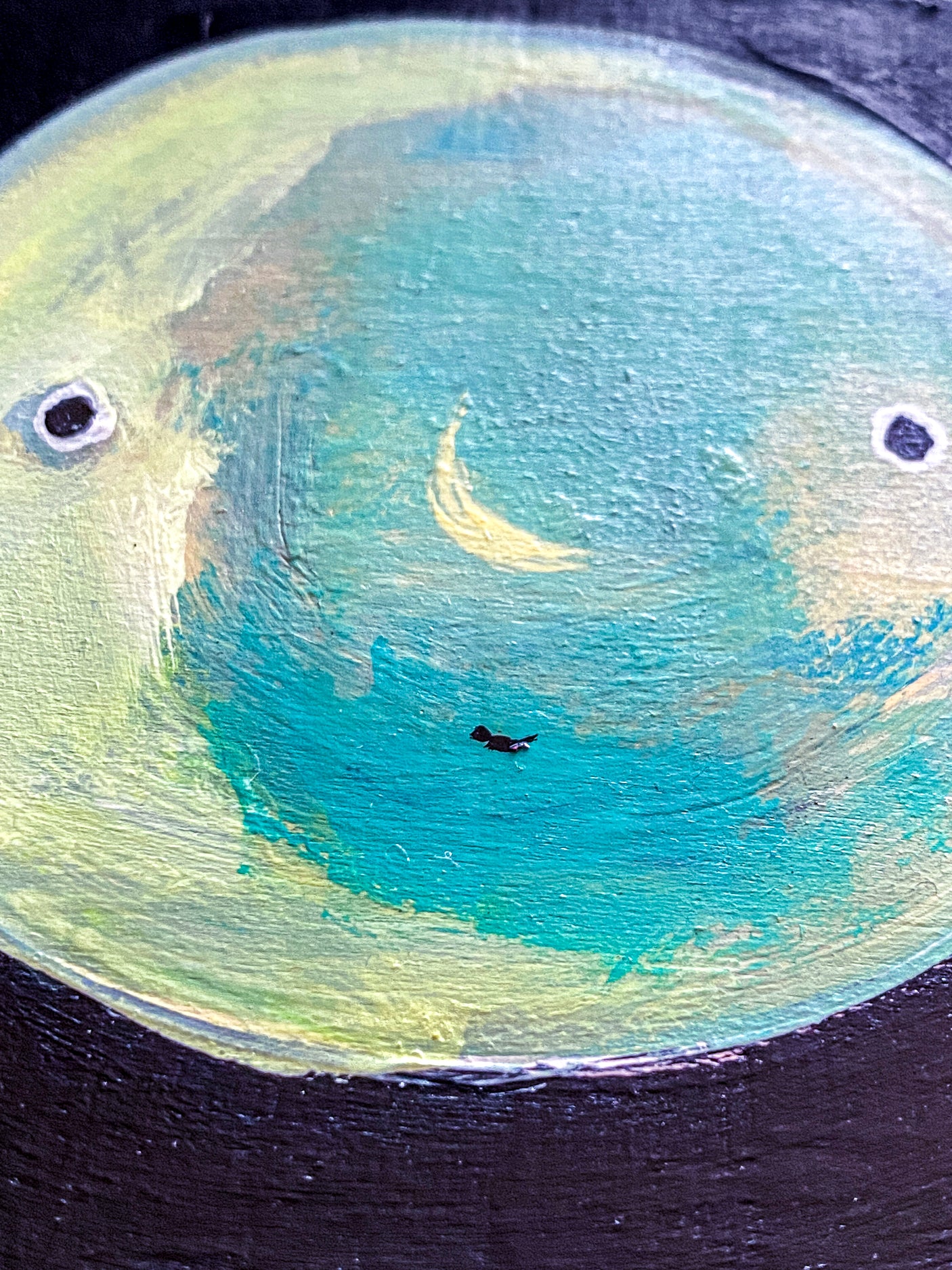 Closeup of painting featuring a blue moon with a subtly drawn face. On one side of the moon, another subtly draw crescent moon appears; artist April Bedard