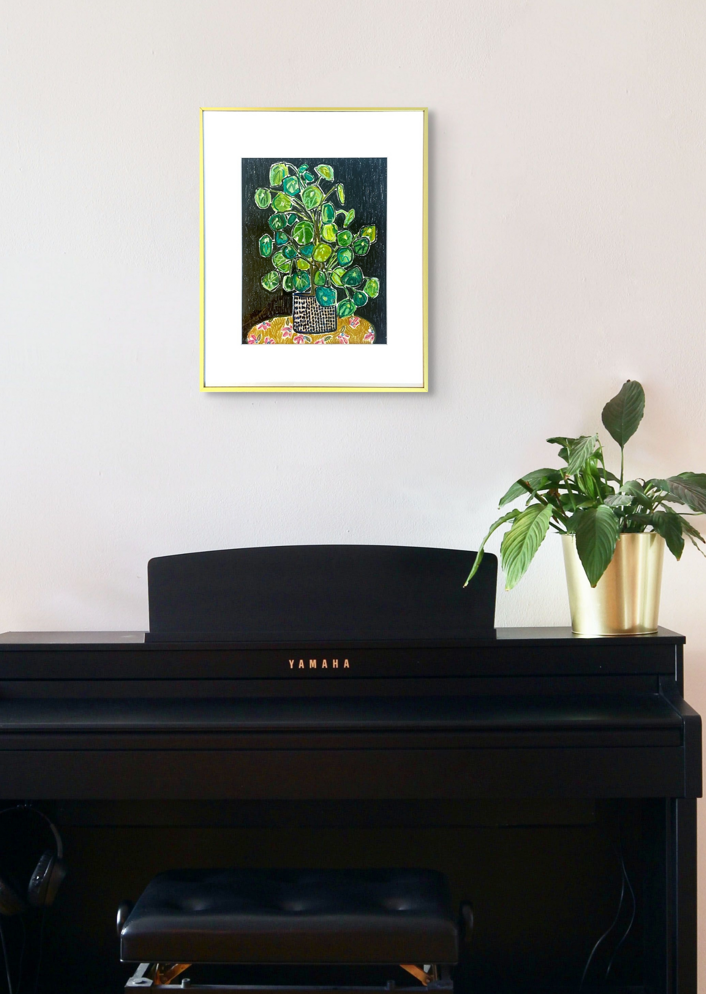 Rachel Bunteman's artwork hangs perfectly over a black upright piano with a small plant on the edge. The metal frame blends with the metal vase.