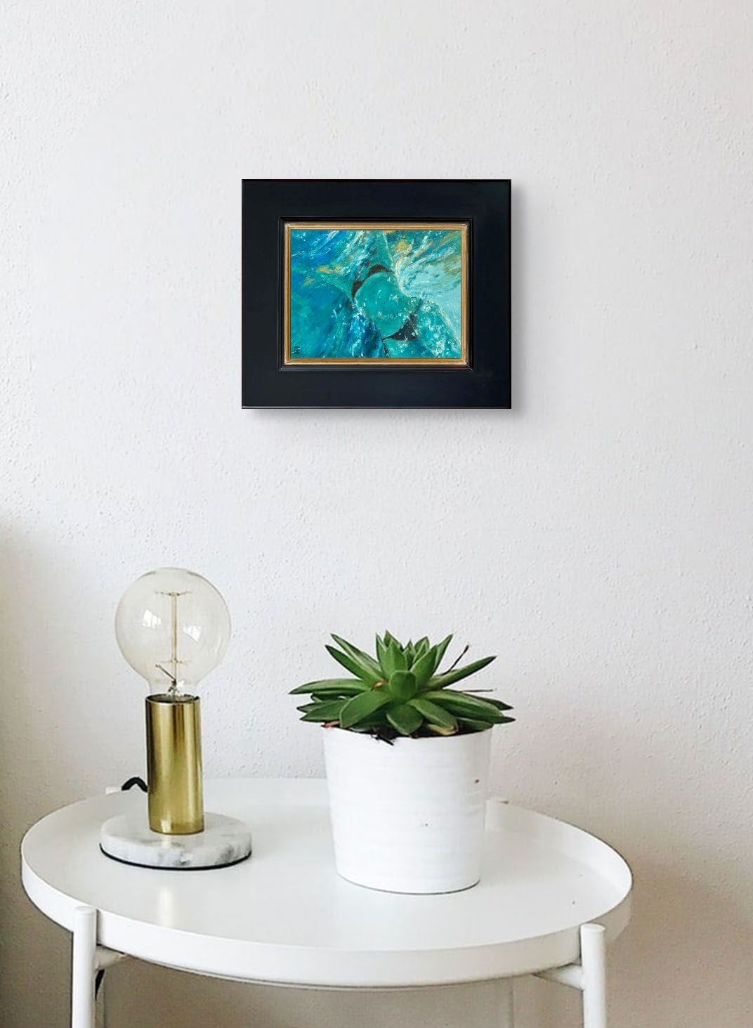 In situ image of Omphalos in its black frame hung on a wall above a small round table with a plant and lamp.