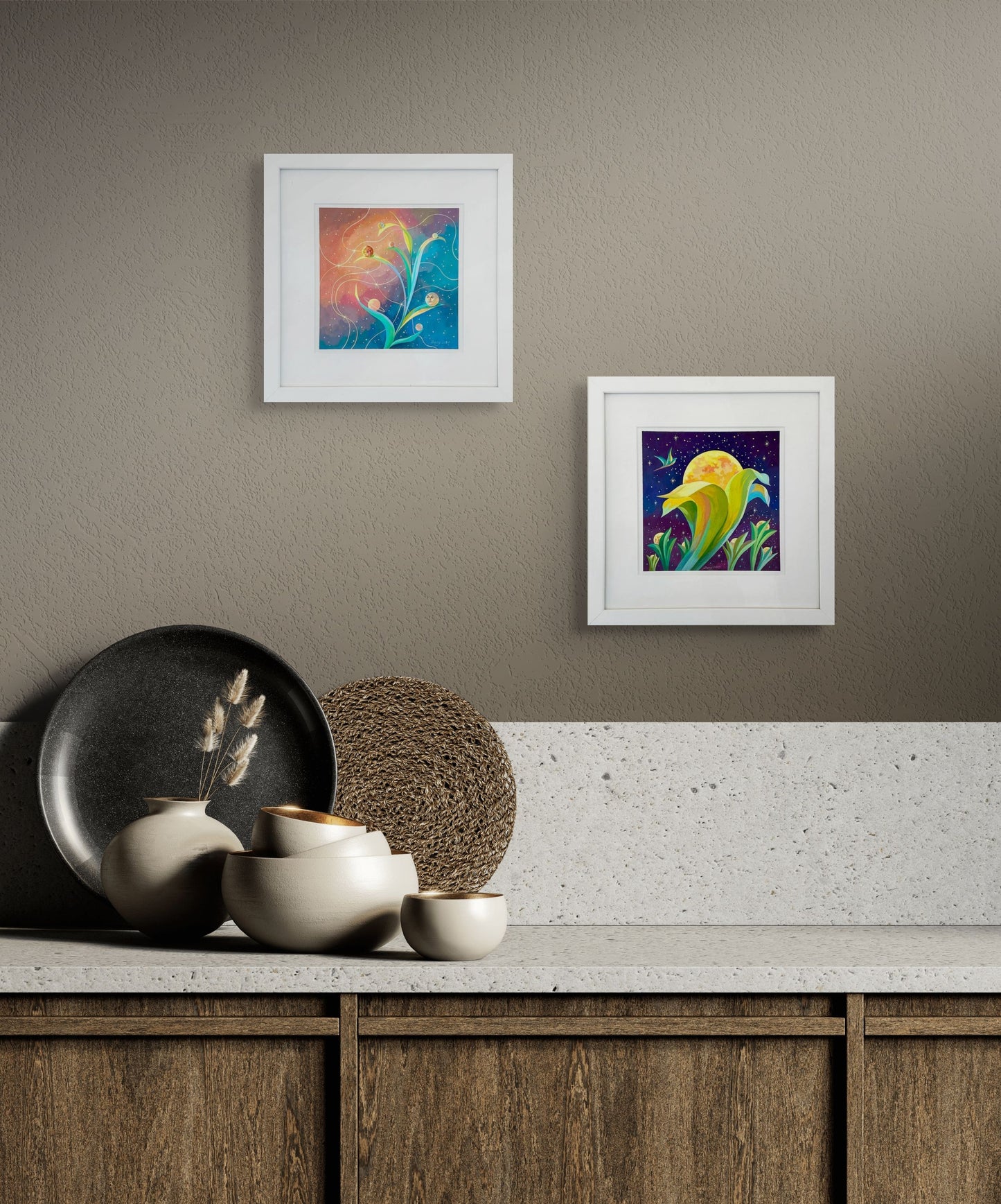 Two of Dany's pieces, Blooming Moons and Planetary Phases hang abouve a counter that is decorated with plates and bowls. The wall is a light gray and the cabinet brown wood with a white granite top.