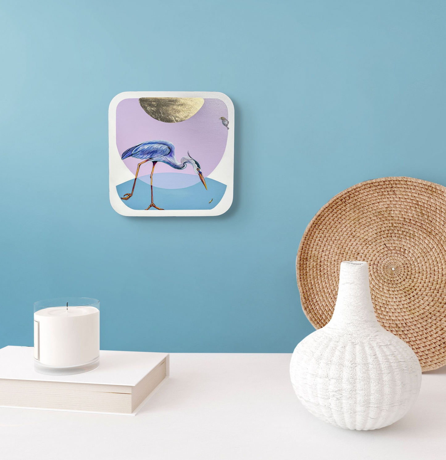 This insitu image shows Spear Fisher hung over a white side table adorned with a small white vase, woven tray, a book and a candle.