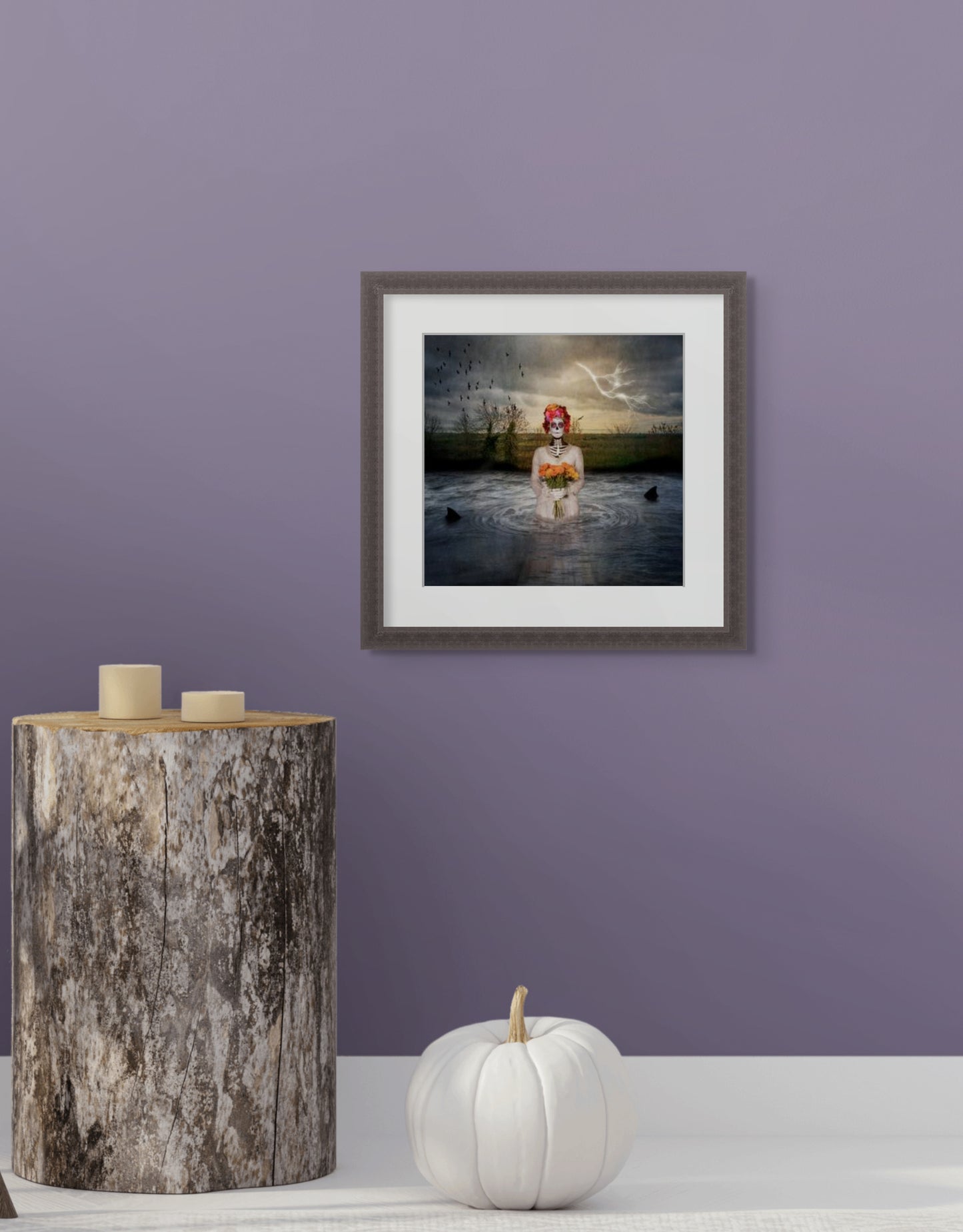 Framed image of  The Catrina on a purple wall with a wooden side table and white pumpkin.