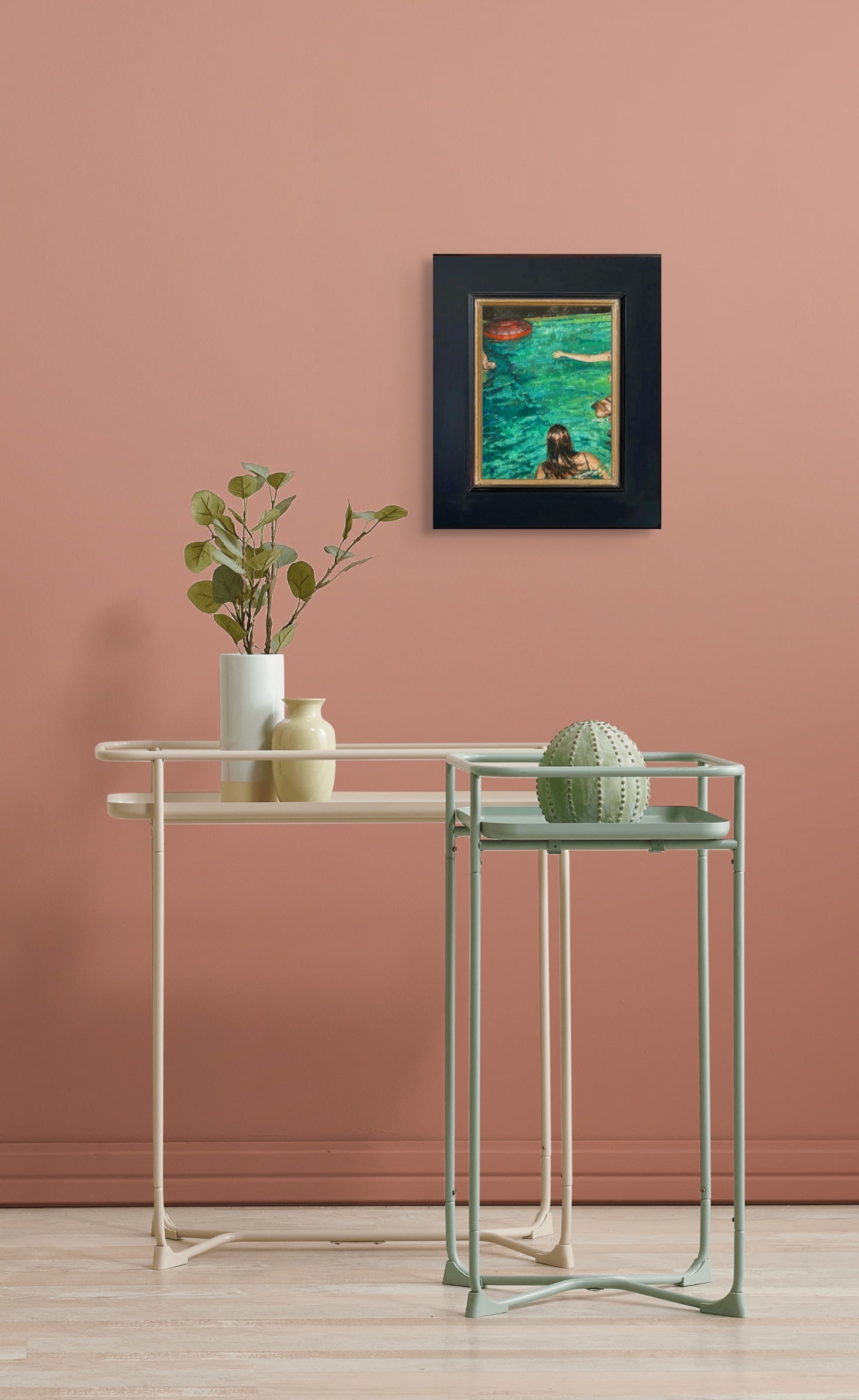 Nesting tables with a plant and decorative item against a pink wall with a Suddenly hanging in its black frame above the stands.