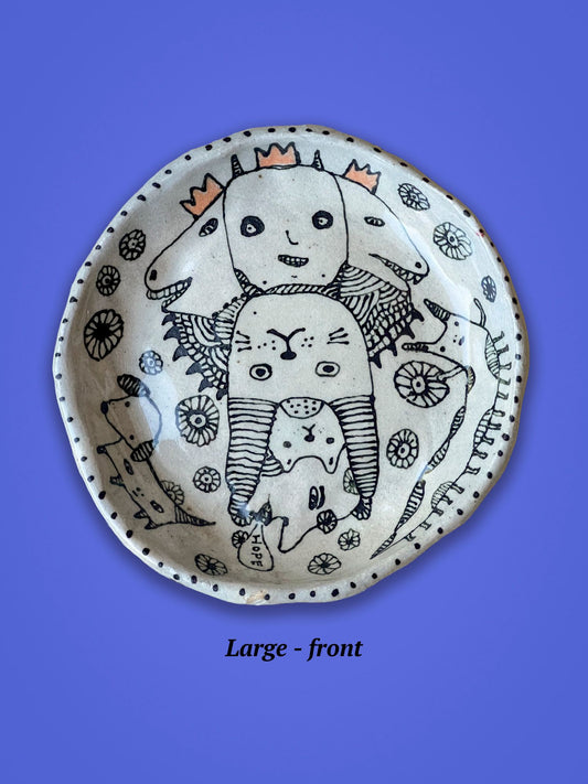 Ceramic bowl with animal illustrations in black ink on a white background. The figures are whimsical animals. Three orange crowns show a spot of color on the piece.
