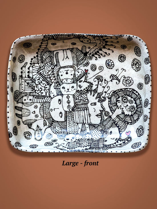 Decorative ceramic plate with black and white patterns on a brown background.There is a wild collection of figures in the center of the plate and a small red heart can be found in the corner.
