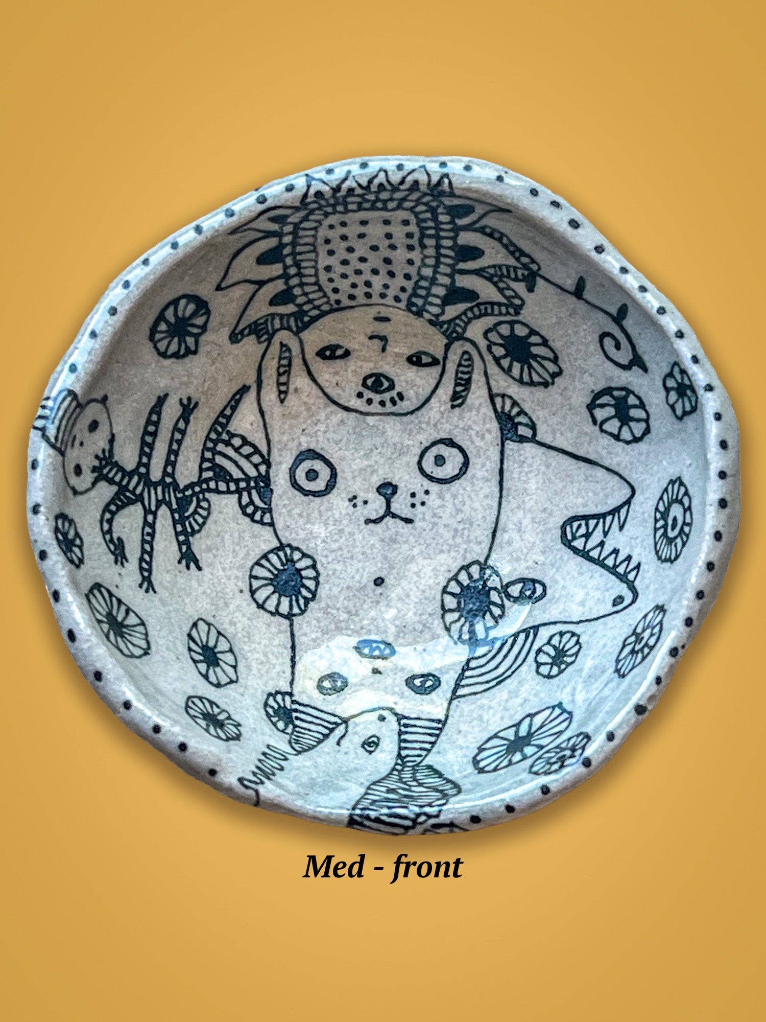 Ceramic bowl with an artistic design of a dog and other creatures. The drawings are black on a white surface. The rim is dotted. 