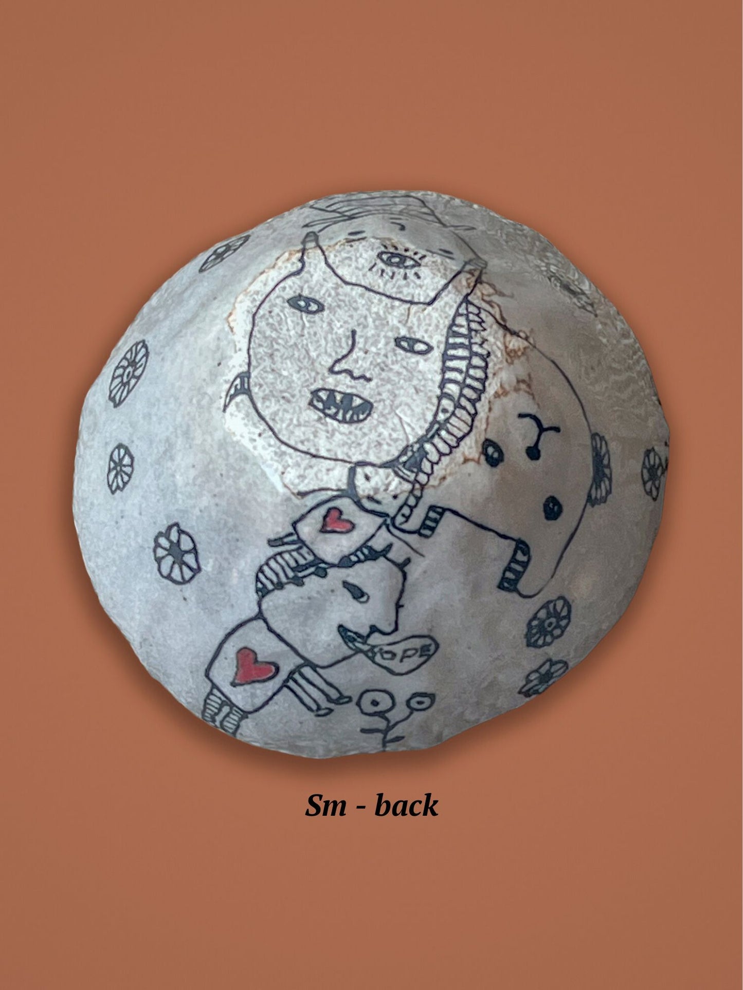 This shows the underside of the previous bowl with a face and heart design. The small hearts are red while the rest is black and white. The bowl rests on an orange background.