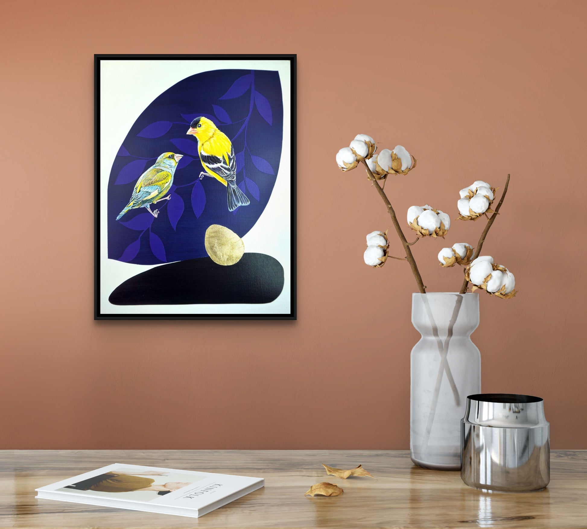 Framed painting of yellow bird and smaller blue bird on blue leaf shaped background in situ. Gold leaf accent; artist Marie Lavallee; 13"Wx13"H