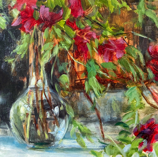 The subject is a clear vase, half full of water which holds a loose vine of red and pink flowers. In the background is an object that glows a bright orange.