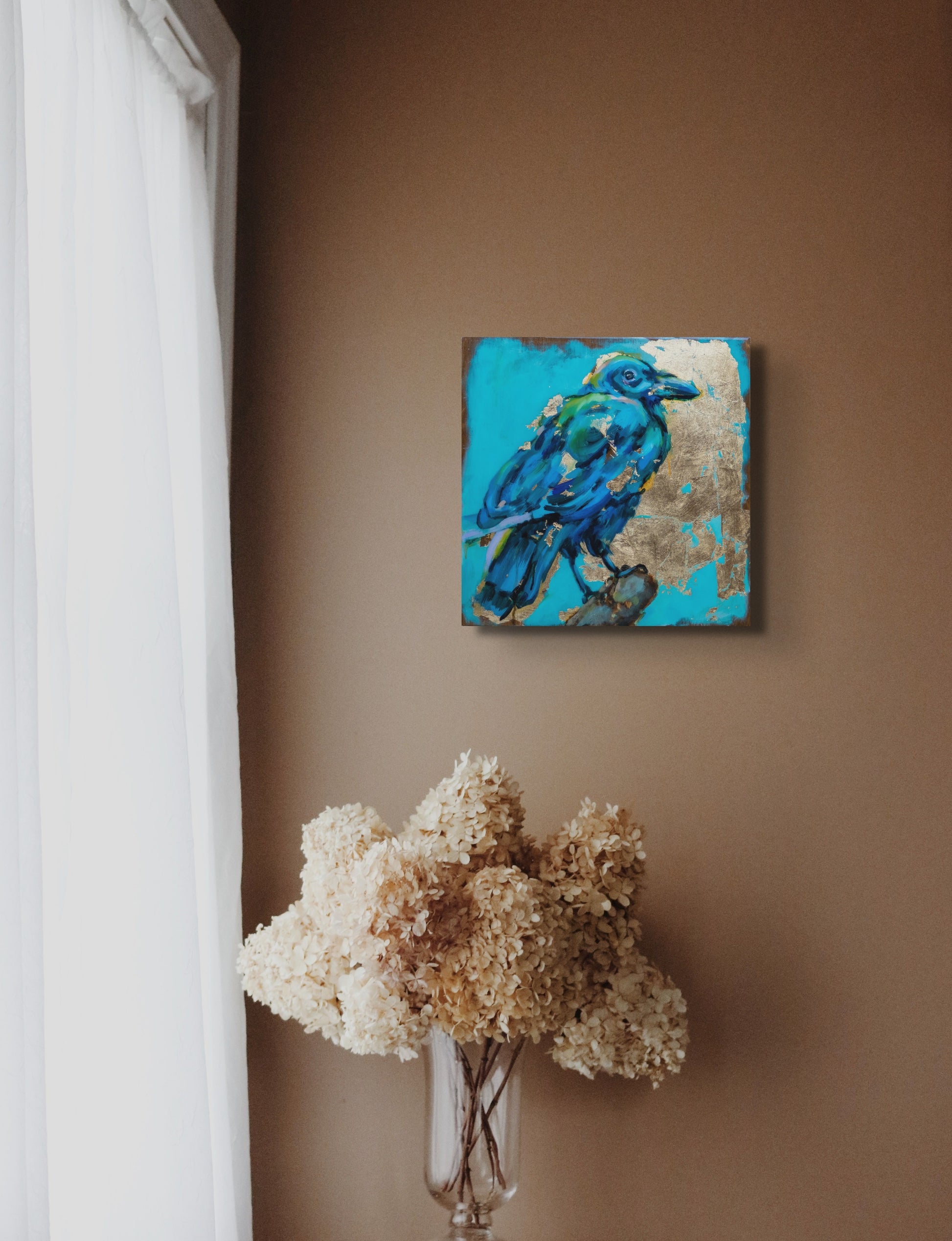 14"x14" painting of Raven using mixed media; acrylic and oil, pencil, and gold leaf with glossy resin finish on surface; shades of blue and gold; artist Shaney Watters; in situ