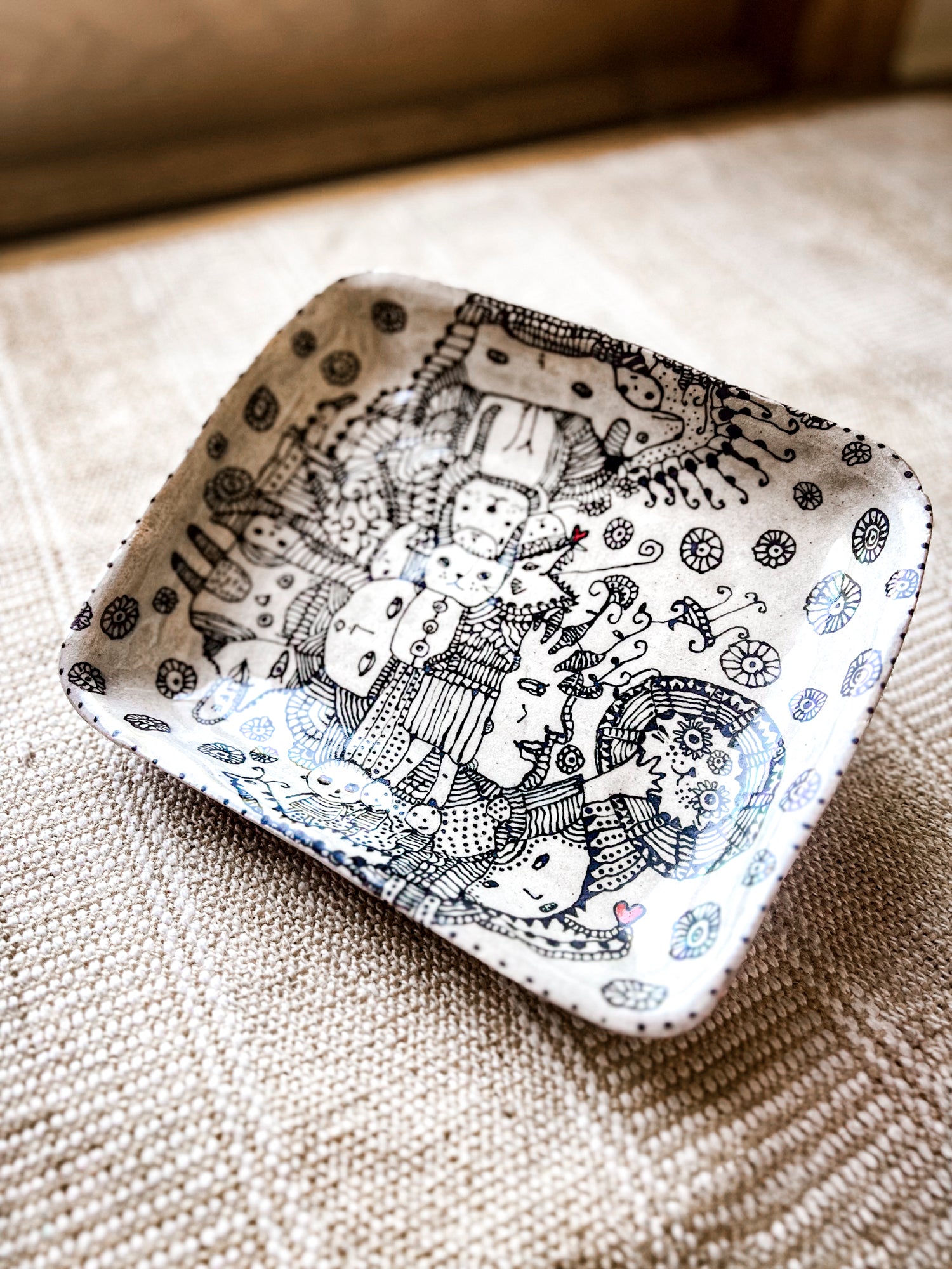 Decorative rectangular plate with black and white intricate designs rests on a stand to show dimensions. The plate is a top a textured surface