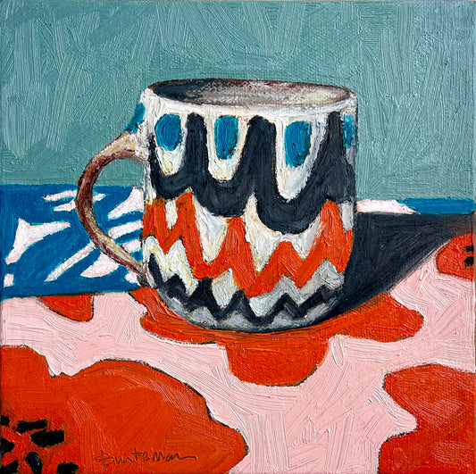 This mug of retro design has a color palette of teal, black, red and white. It coordinates with the table top it sits upon and a teal background wall. The design is scalloped rows of color. 