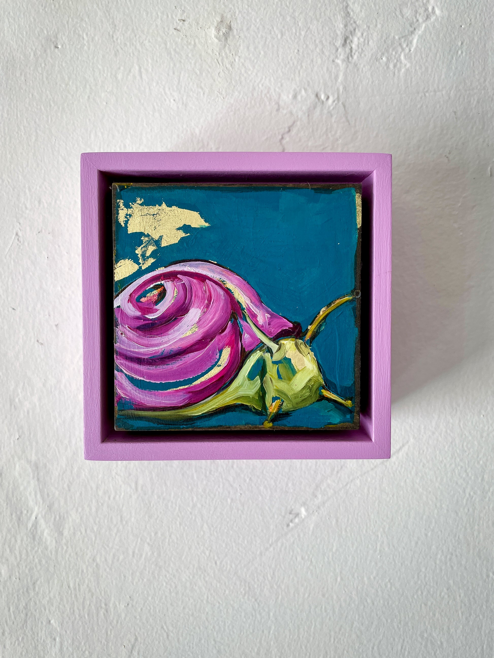 Colorful whimsical painting of a snail in blues and purples with touch of gold leaf; 5"x5" incl painted frame; artist Shaney Watters; shown on wall in situ