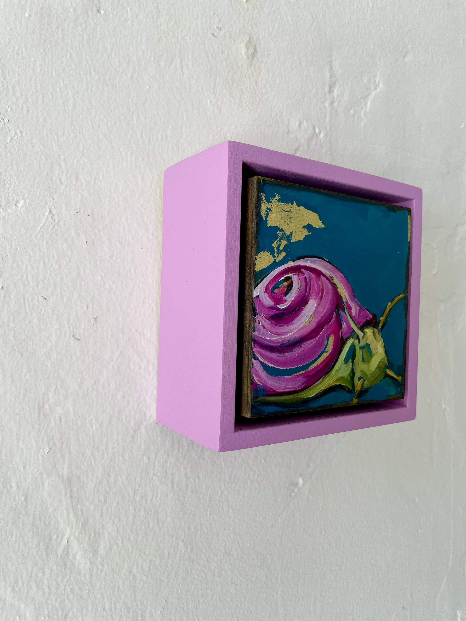 Colorful whimsical painting of a snail in blues and purples with touch of gold leaf; 5"x5" incl painted frame; artist Shaney Watters;  shown on wall, side view