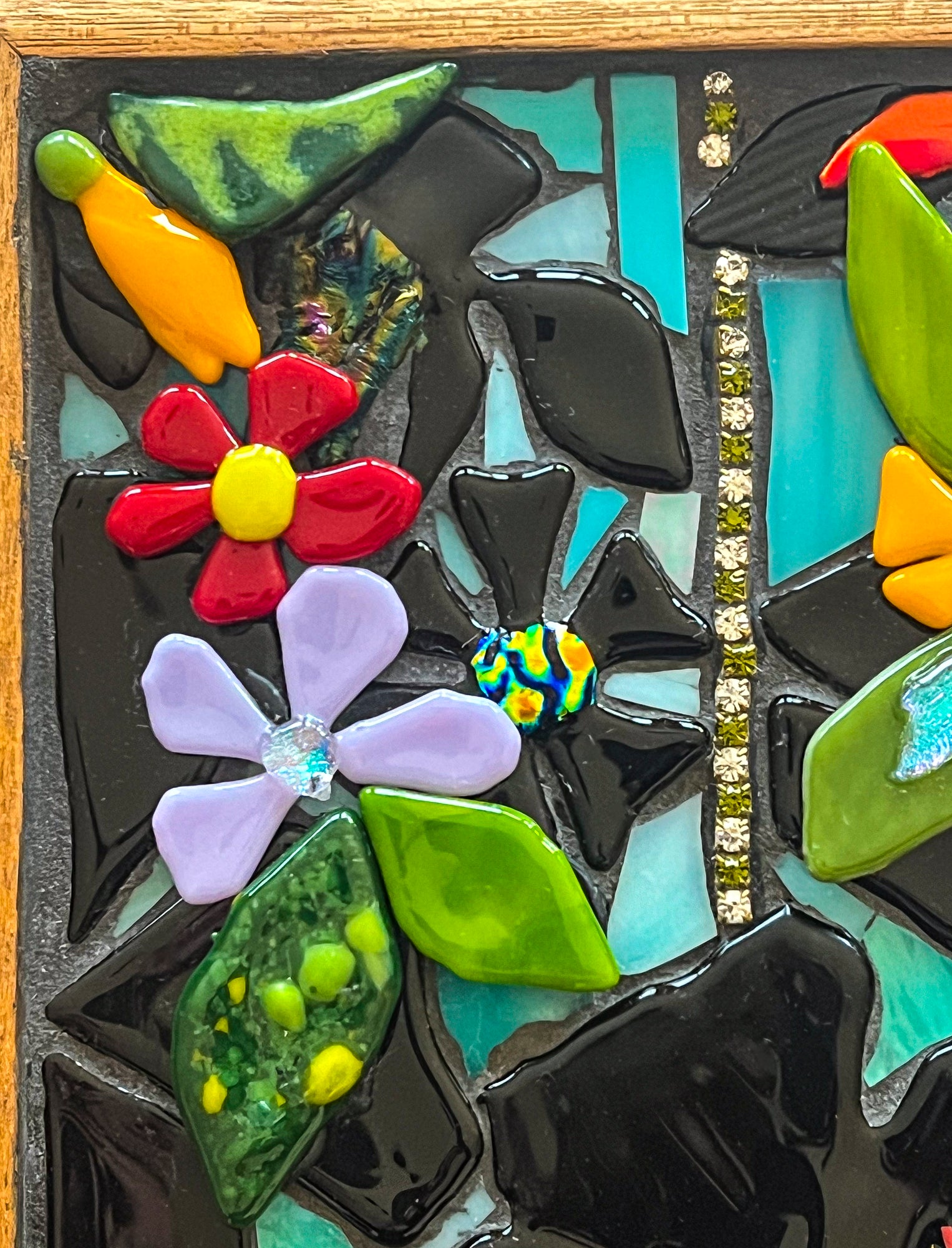 Closeup of glass mosaic artwork of leaves and flowers using fused glass of black interspersed with bright colors;  artist Denise Marshall