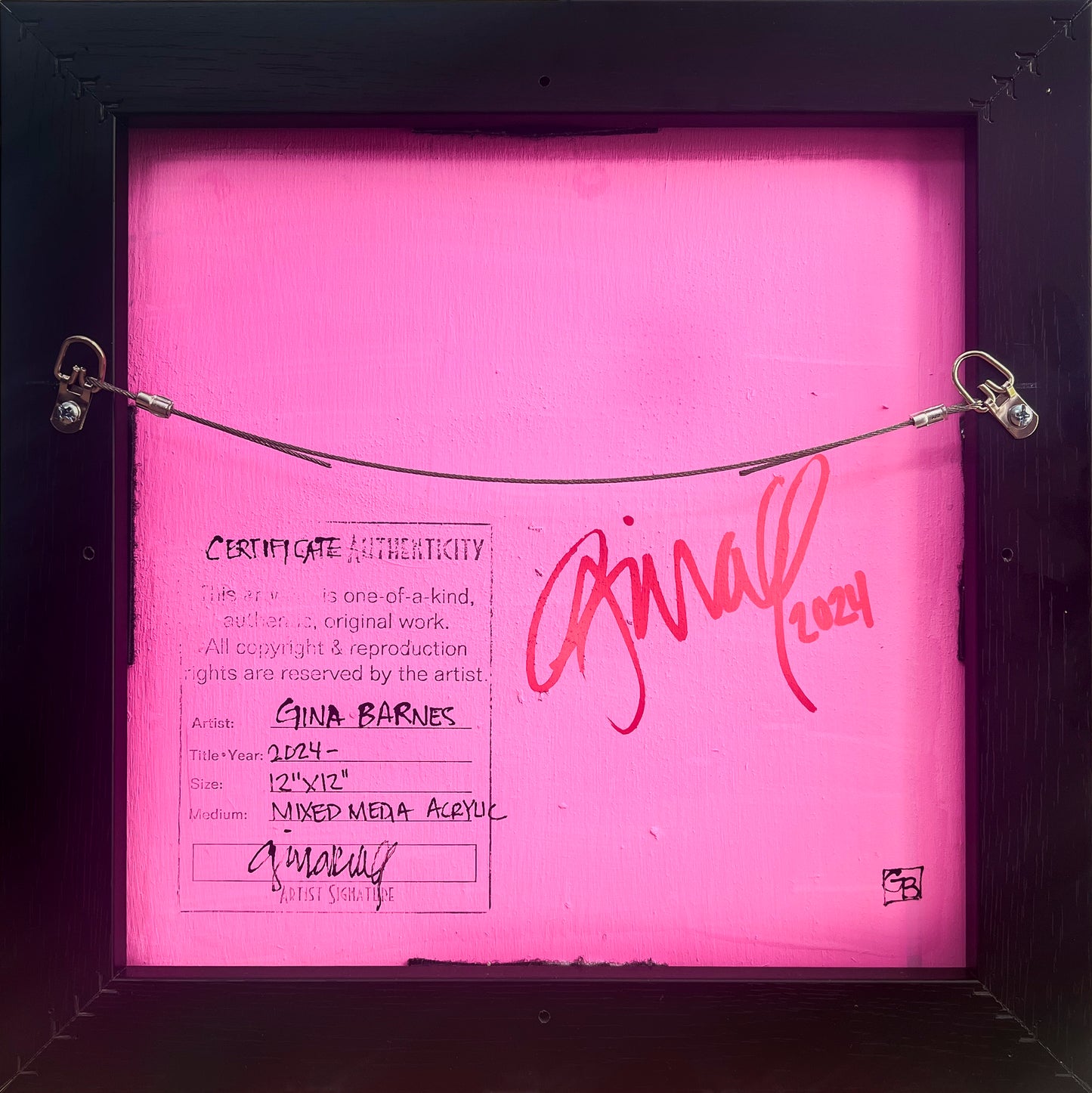 View is the back of the painting which shows Barnes' signature pink backing with her signature and certificate of authenticity. Also shows the wire hanger.
