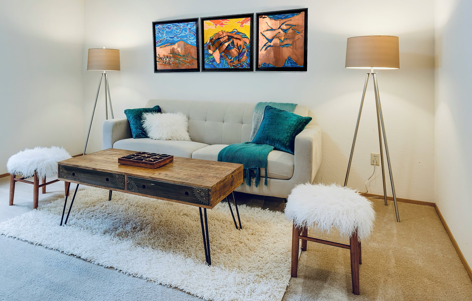 In situ shot of a living room with the Ocean Swept Away, The Ocean Within and Mountain Sea hanging as a set above the couch. The room has two standing lamps, a coffee table and two small chairs. The wall is white. 