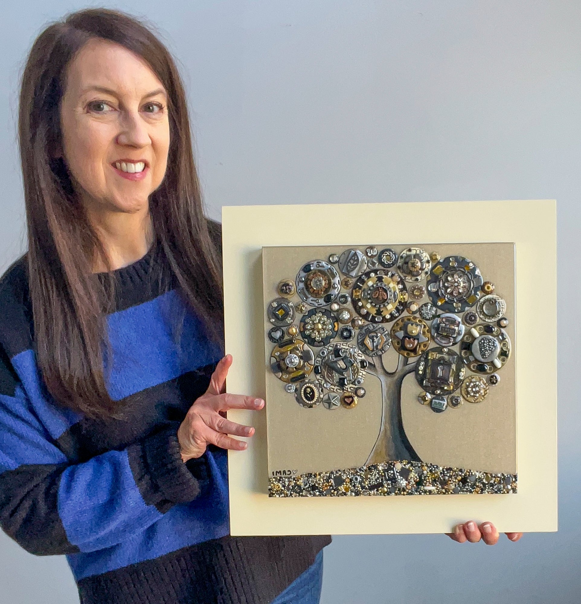 Here the artist Cami Levin holds her framed piece showing the dimensions. The work is framed on an ivory painted wooden board. 