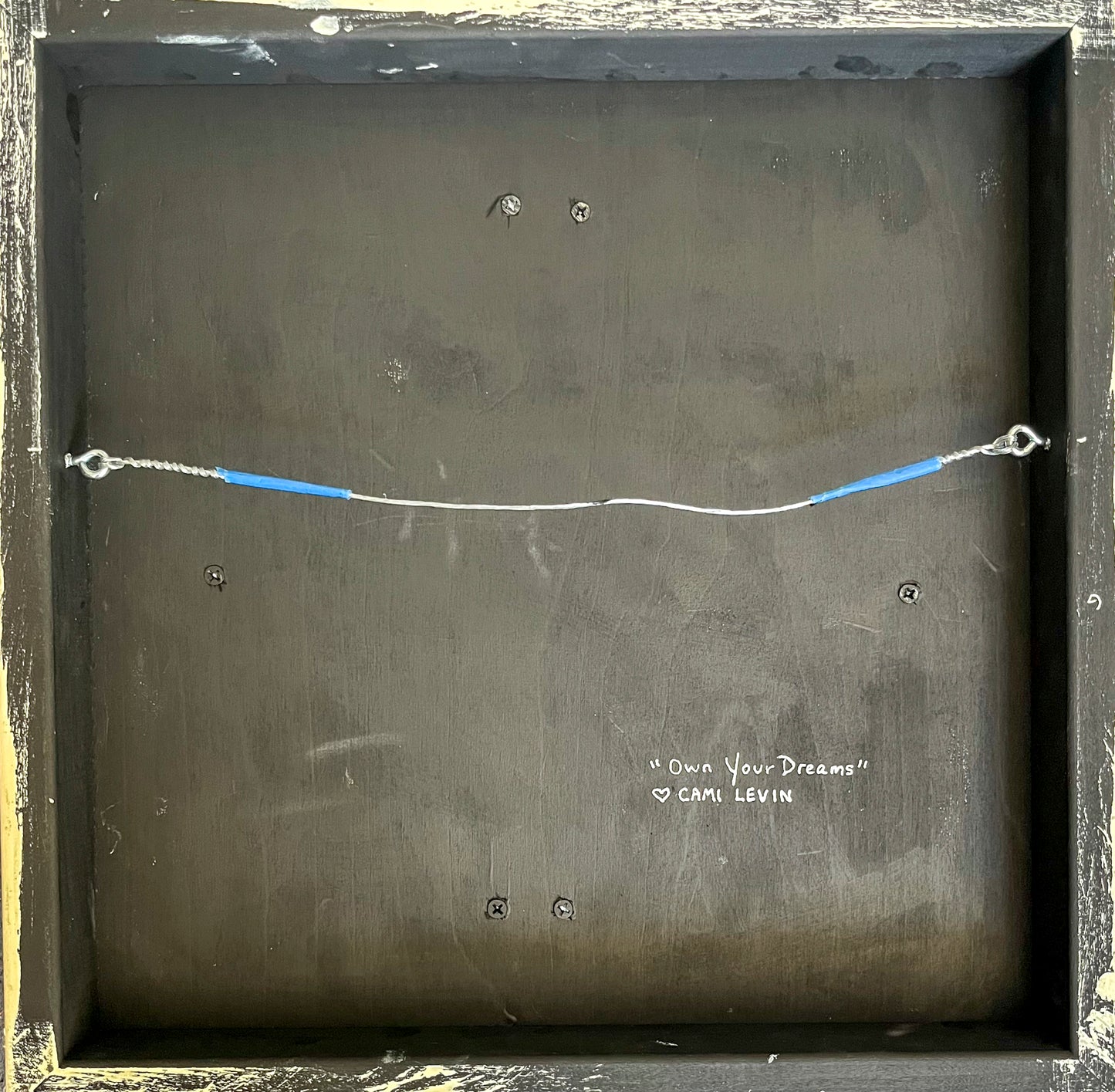 Back view of the piece shows a wire hanger and artist's signature. 