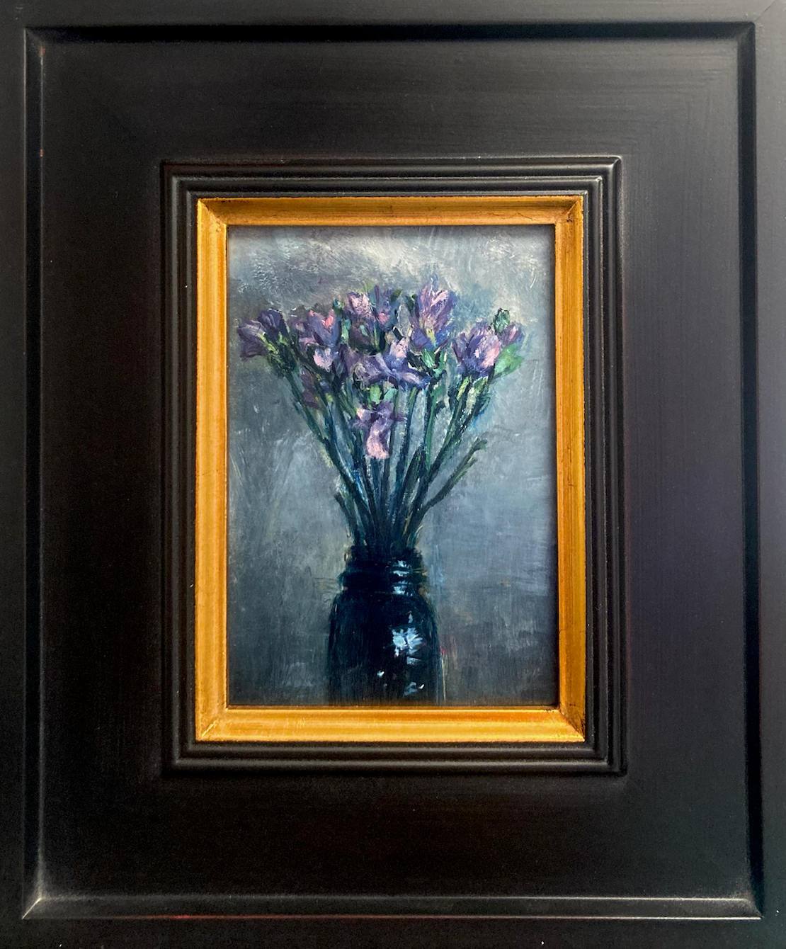 Oil painting of purple flowers in a black vase against a gray background titled 'Purple' by E. E. Jacks with dark wood frame with gold trim