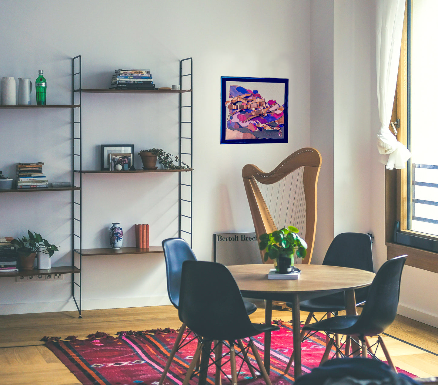 This in situ photo shows Switchbacks on a white wall next to a wire bookshelf. The room has a small dining table rug and light is coming in from a large window. 